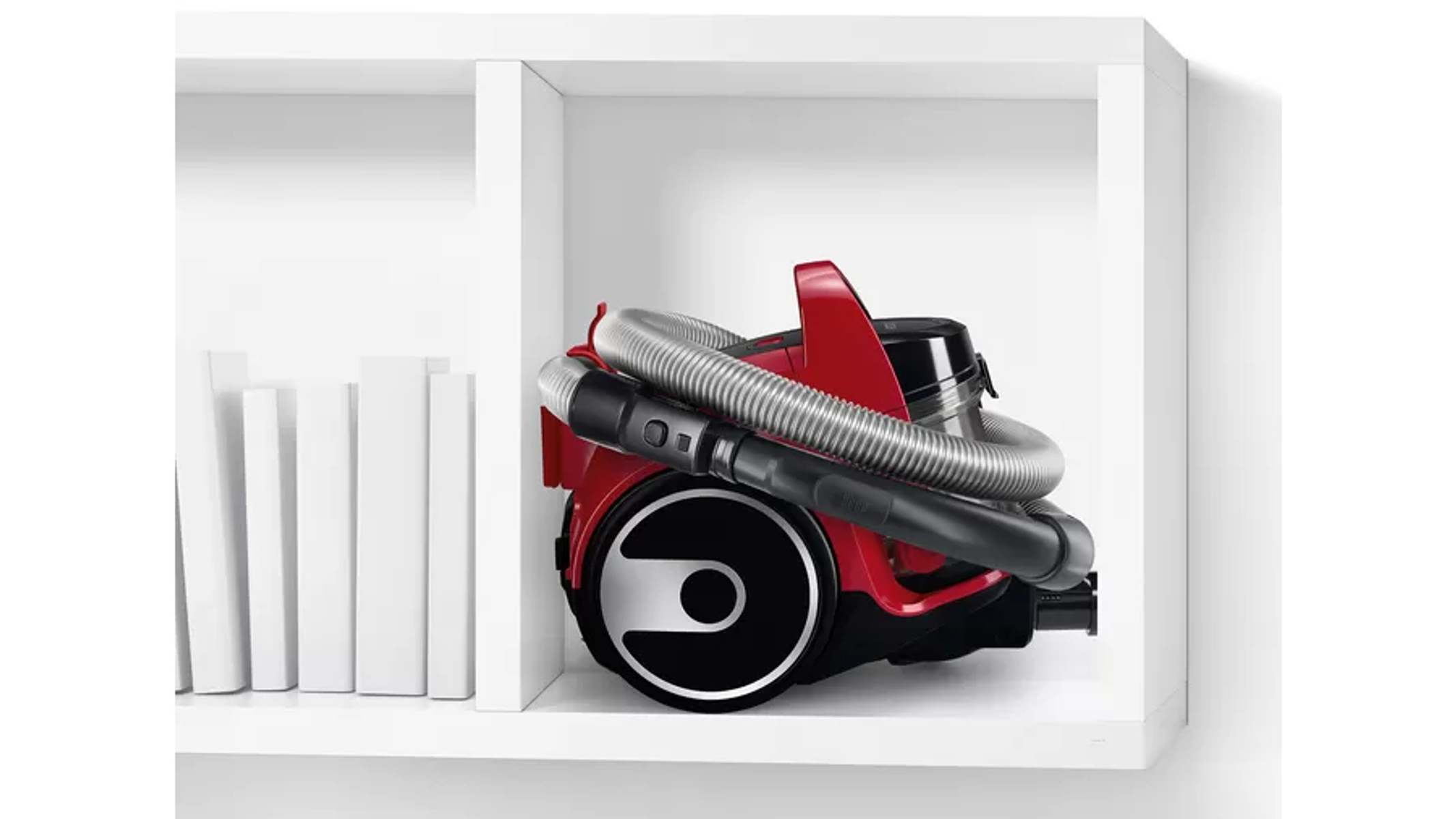 Czerwony odkurzacz jest przechowywany wewnątrz białej półki.