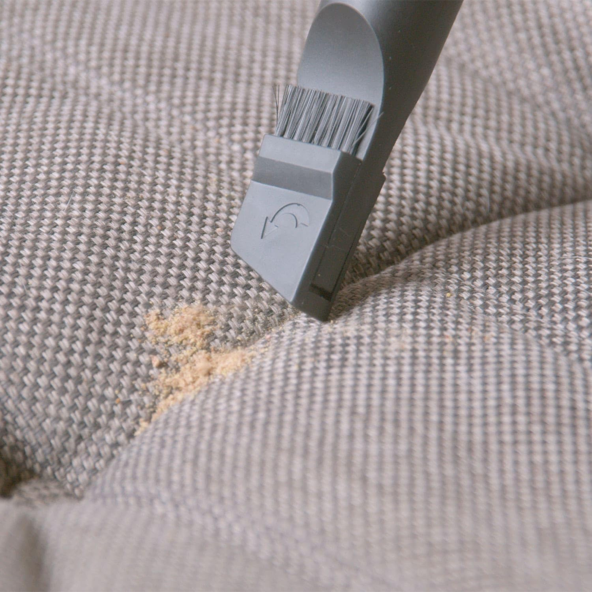 Zbliżenie odkurzacza czyszczącego sofę. Na sofie jest brud.