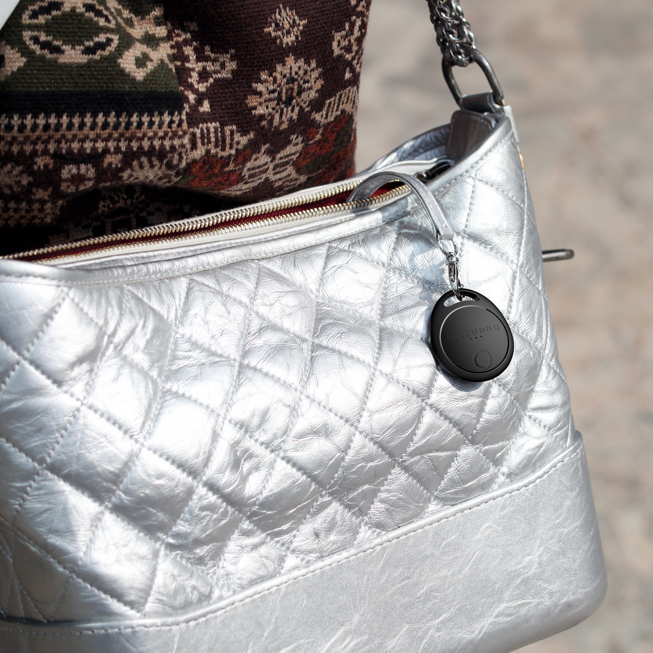 Silberne Stepptasche mit einem schwarzen, runden Anhänger. Nahaufnahme.