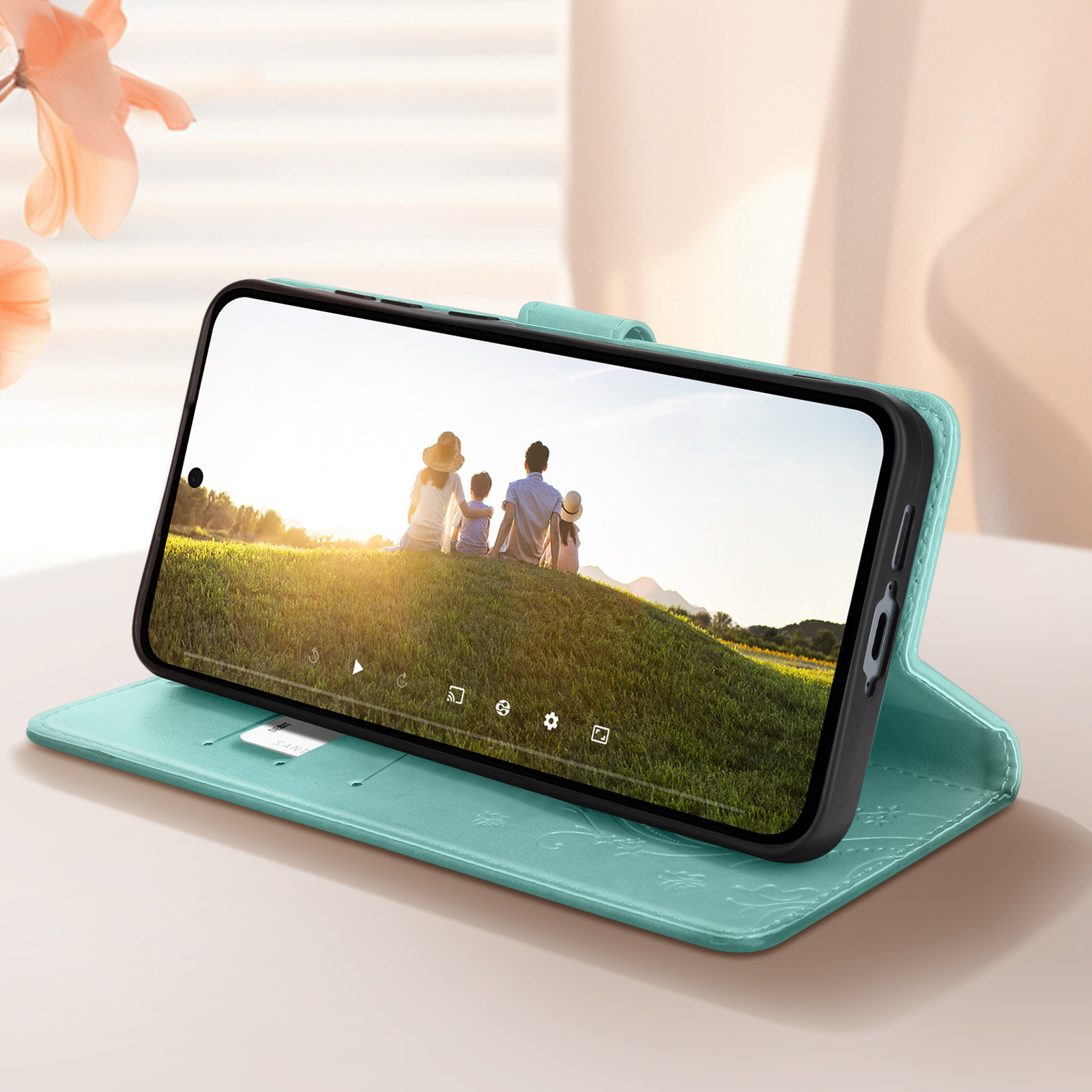 Un telefono in una custodia turchese mostra una foto di famiglia su un prato verde.