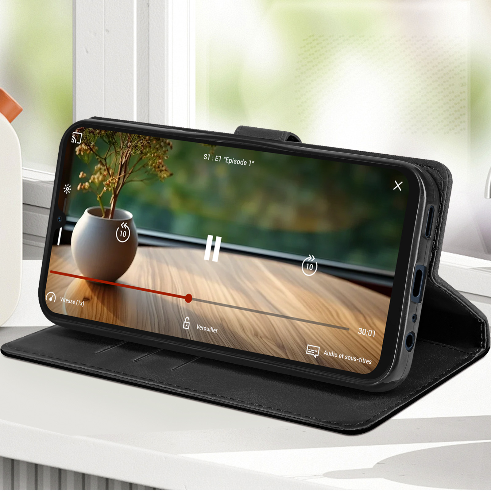Ein Smartphone in einer schwarzen Hülle, das ein Video zeigt. Eine kleine Pflanze steht in einer Vase auf dem Holztisch.