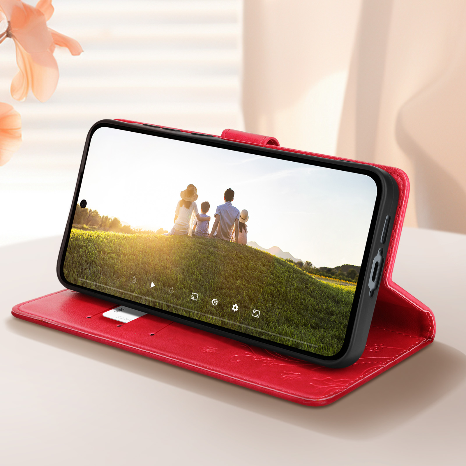 Custodia rossa con telefono che mostra famiglia su collina verde.