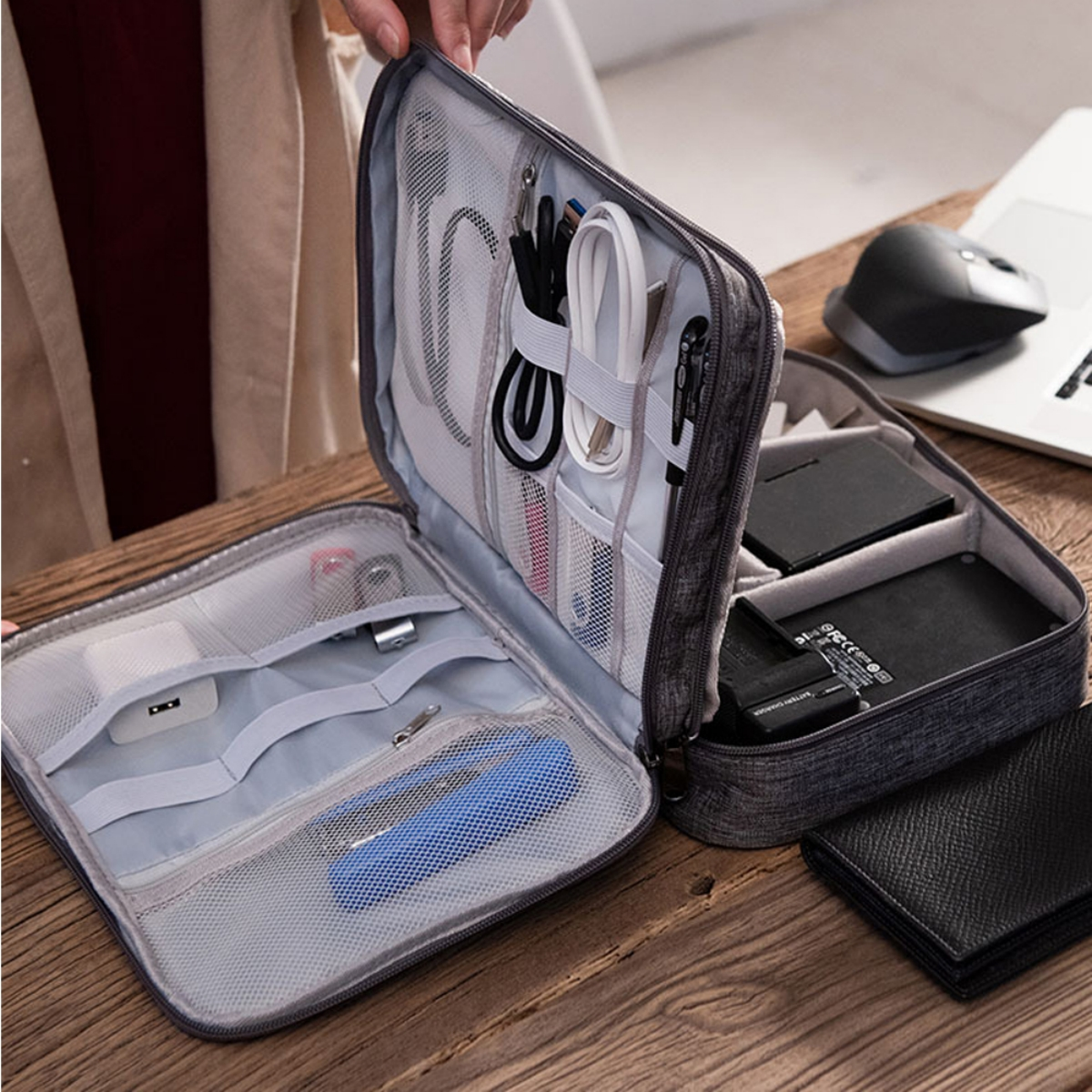 Eine graue Reise-Organizer-Tasche geöffnet. Darin befinden sich verschiedene technische Accessoires wie Kabel und Ladegeräte.
