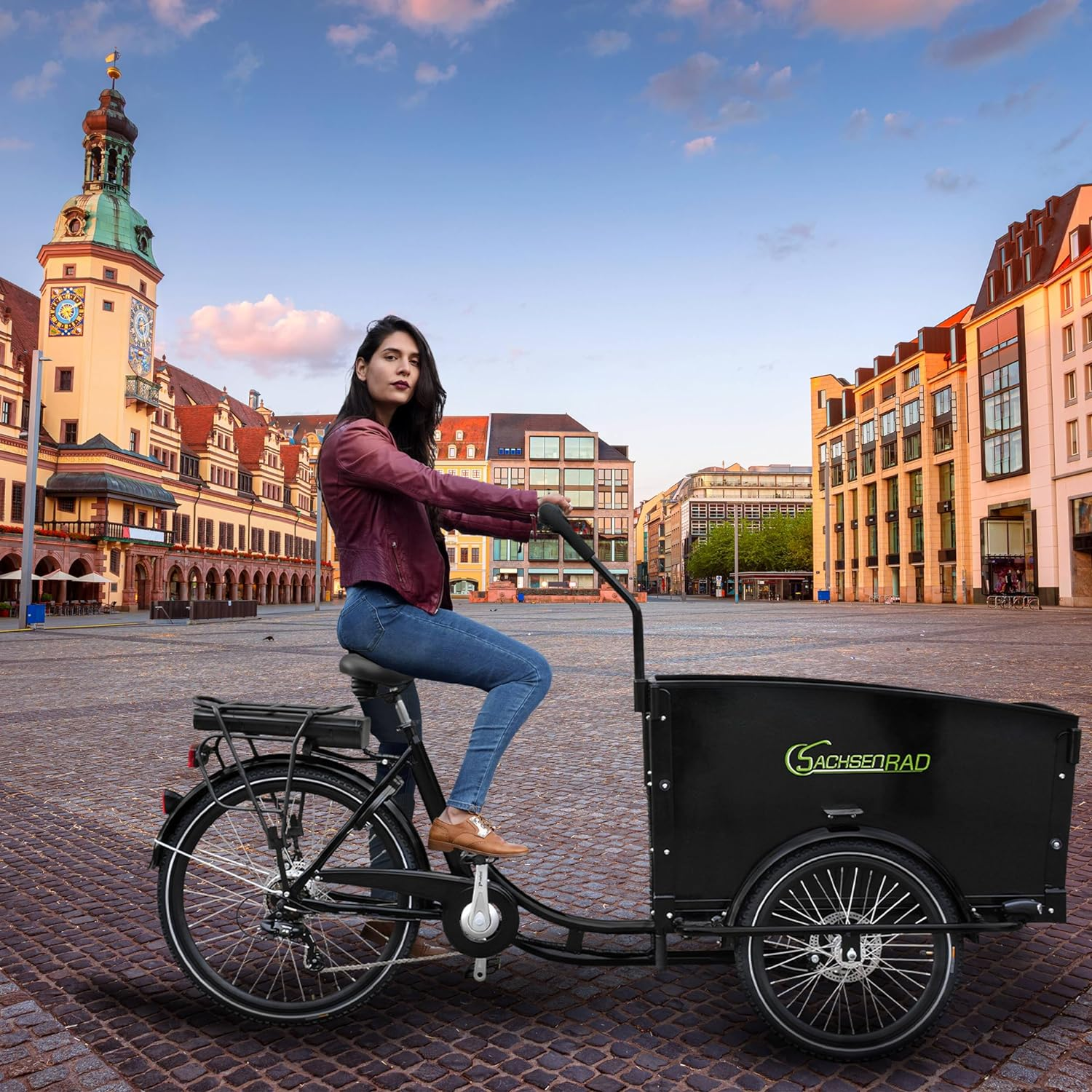Eine Frau fährt mit einem schwarzen Lastenrad auf einem Kopfsteinpflaster.