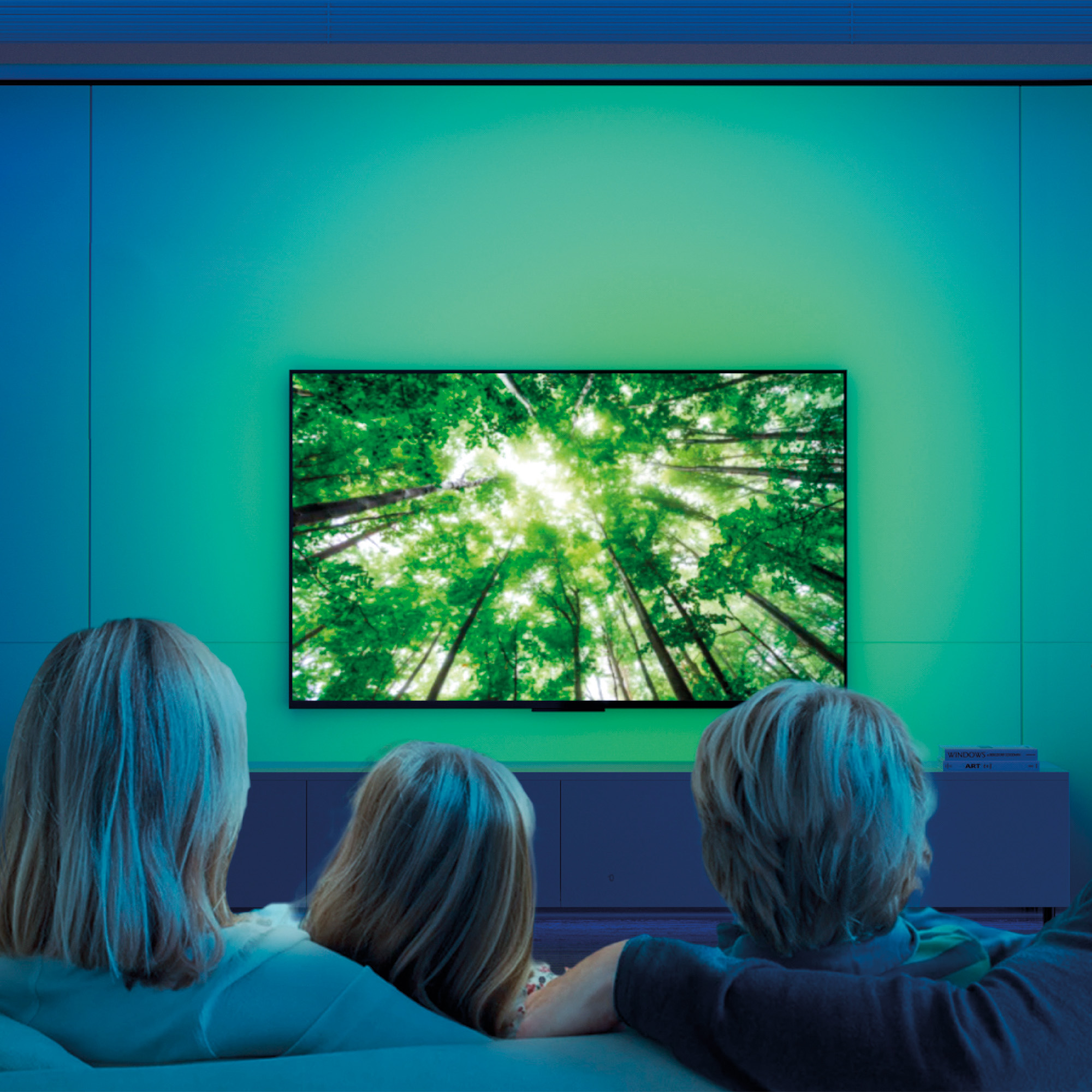 Tres personas sentadas en un sofá mirando una TV con una escena de bosque verde.