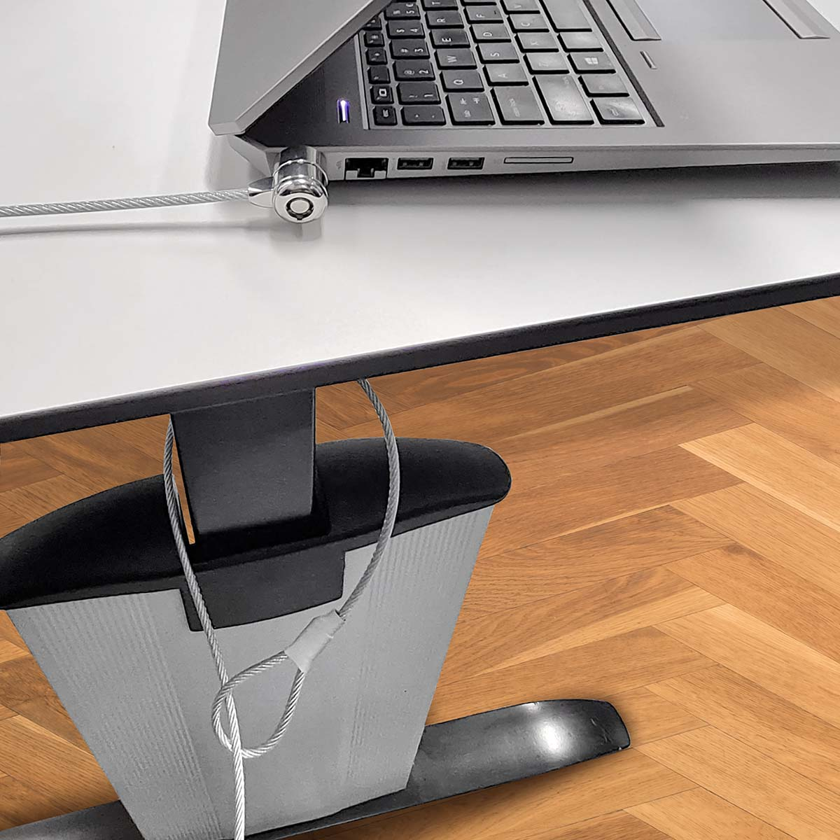 Laptop protetto con un lucchetto a cavo attaccato a una gamba del tavolo. Lo sfondo è un pavimento in legno.
