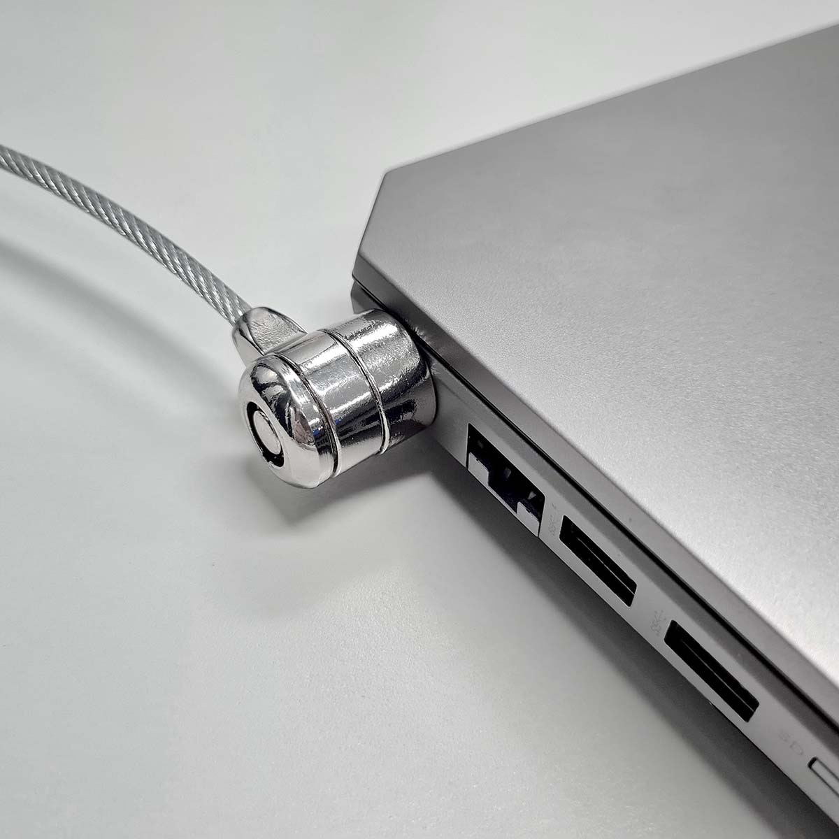 Laptop argentato assicurato con un lucchetto a cavo su una superficie bianca.