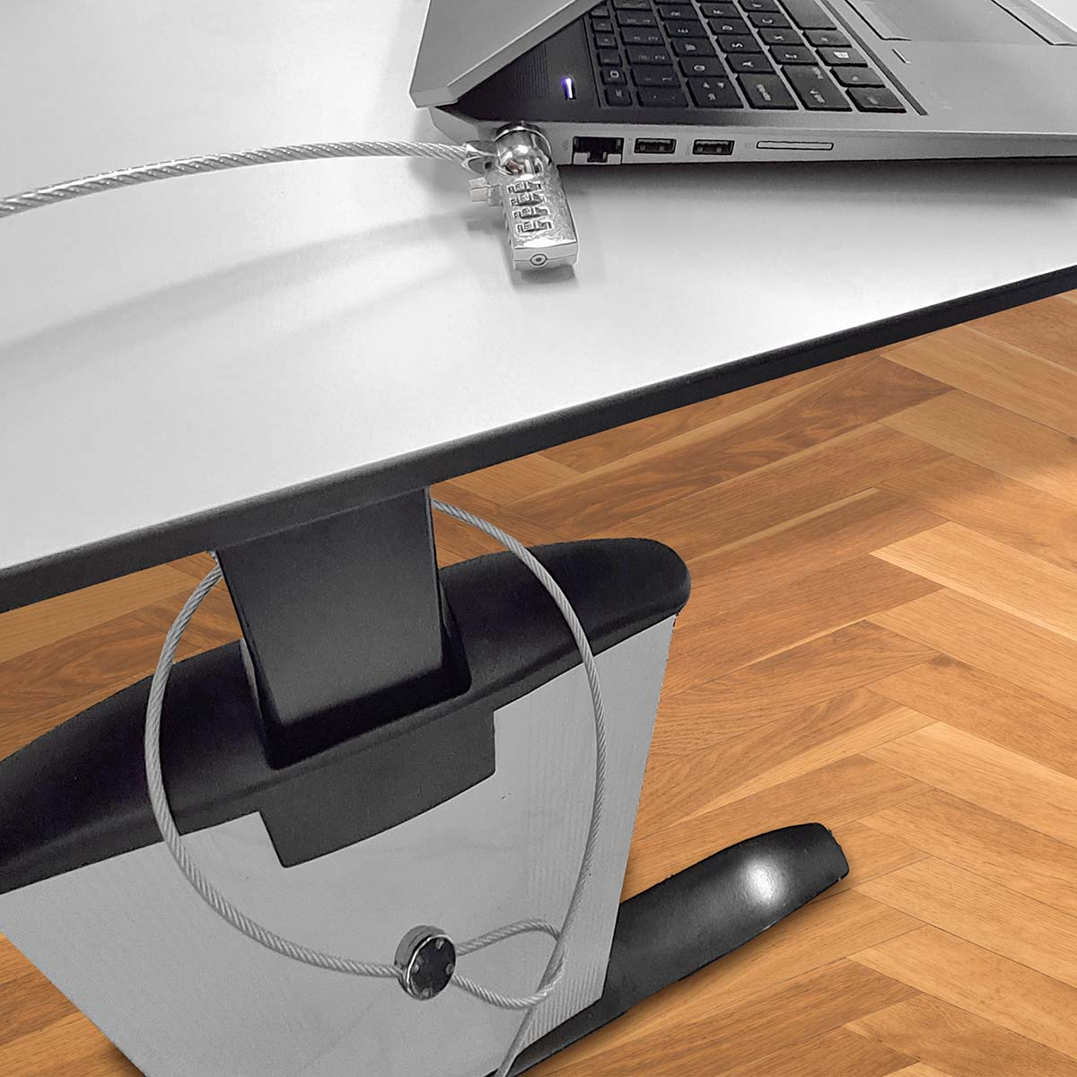 Ein Laptop mit Kabelschloss auf weißer Oberfläche gesichert, in der Nähe eines Holzbodens.