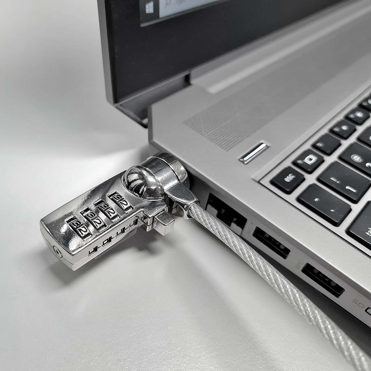Laptop mit silbernem Zahlenschloss und Kabel gesichert. Das Schloss befindet sich an der Seite.