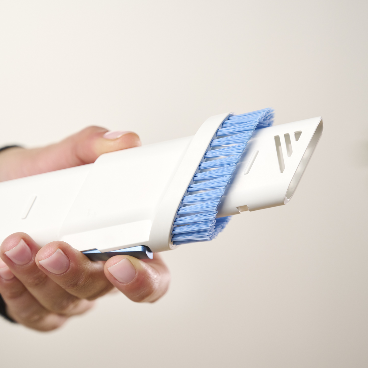 Una mano che tiene un accessorio per aspirapolvere con setole blu. L'accessorio è bianco.