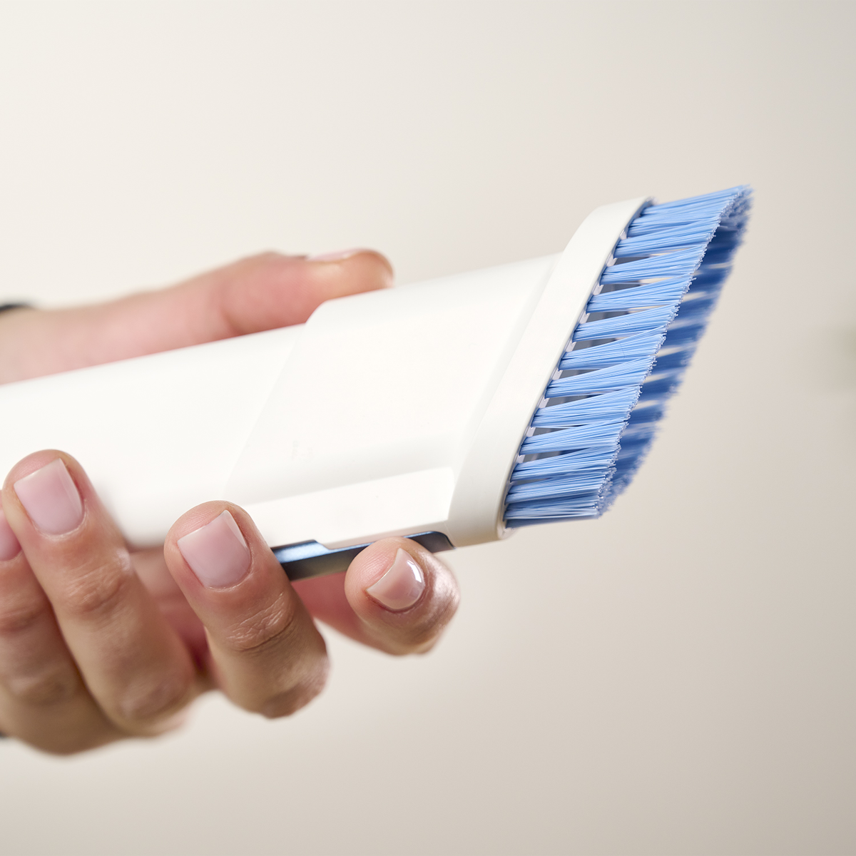 Primo piano di una mano che tiene un accessorio per aspirapolvere bianco con setole blu.