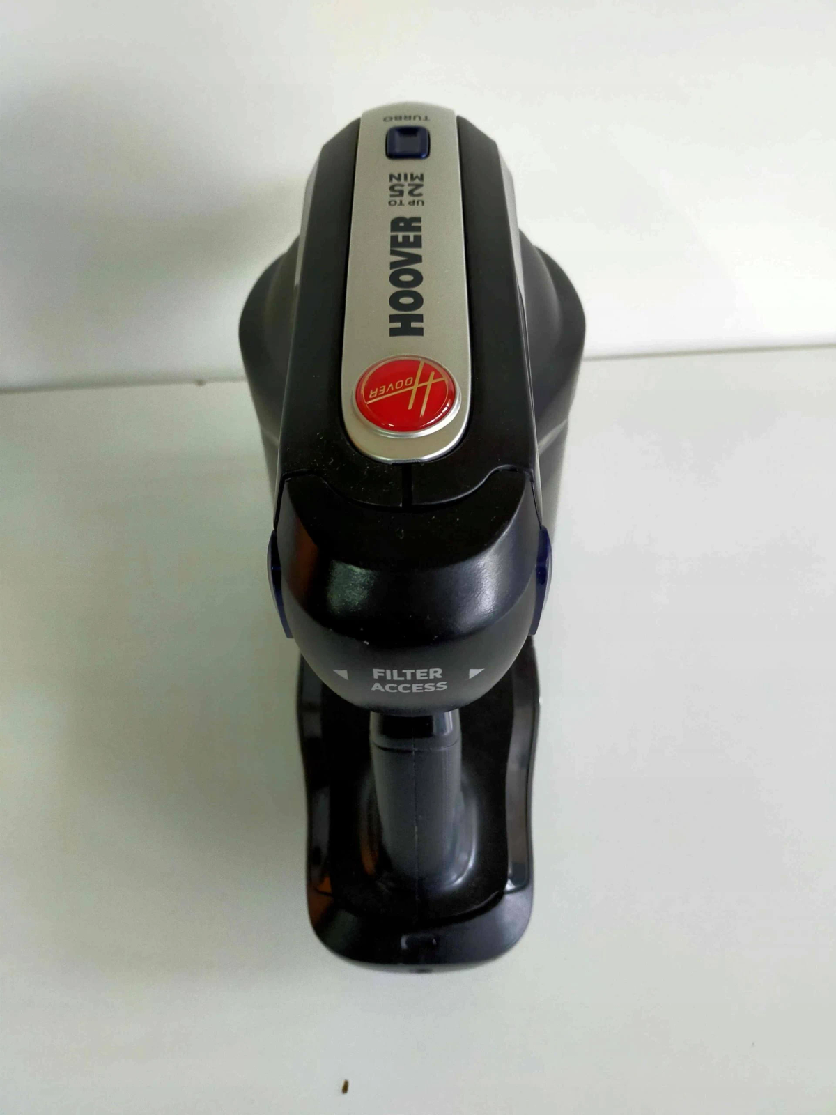 Una vista dall'alto di un aspirapolvere portatile Hoover nero. Ha un pulsante di accensione rosso e accesso al filtro.
