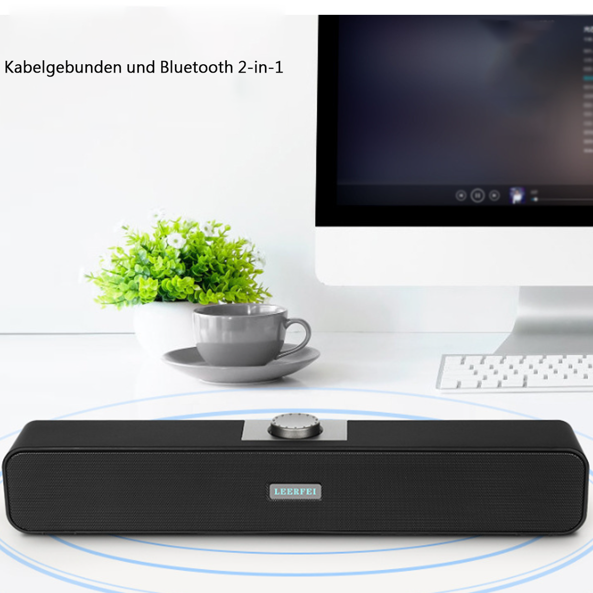 Schwarze Soundbar auf einem Schreibtisch. Text oben: 'Kabelgebunden und Bluetooth 2-in-1'. Pflanze und Monitor im Hintergrund.
