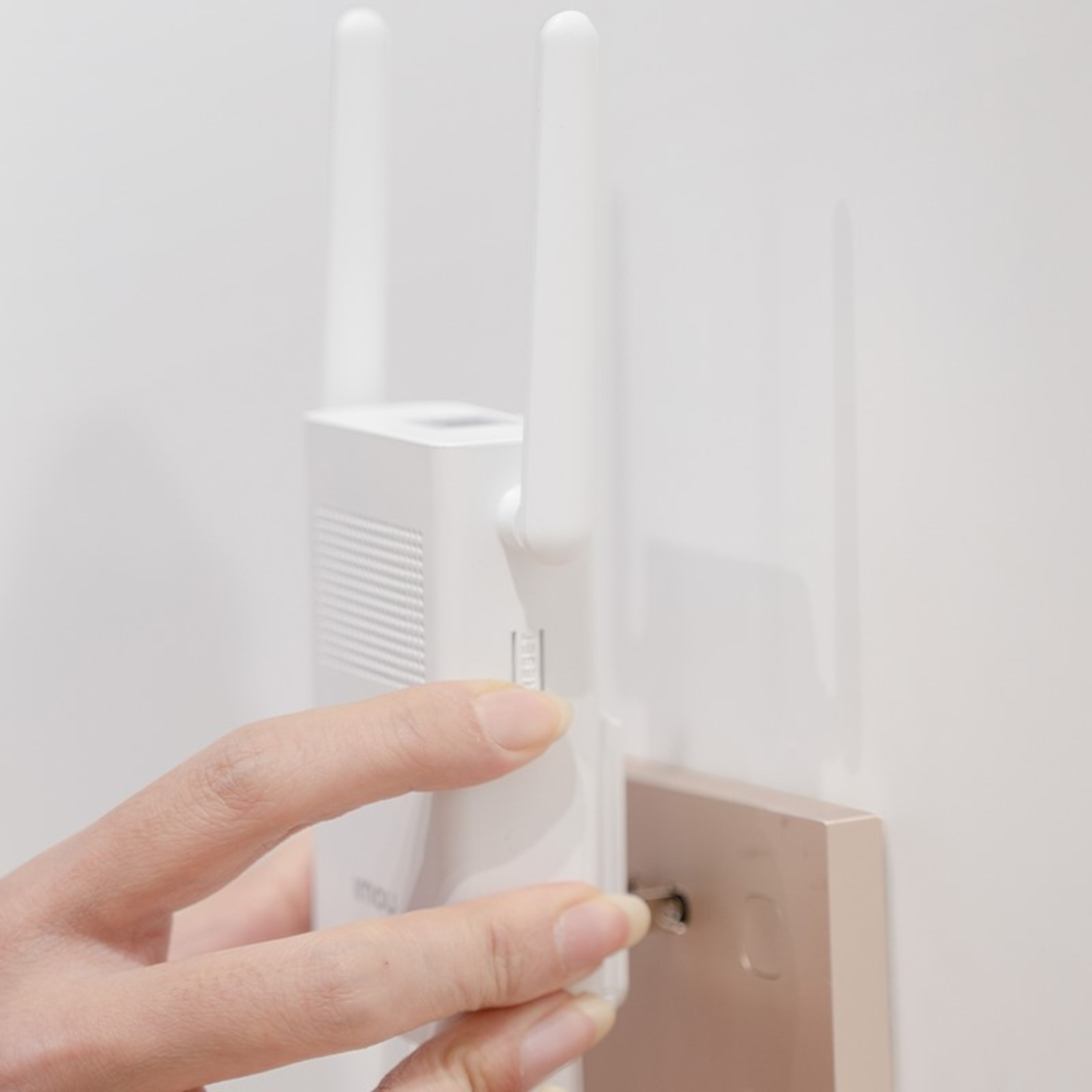 Una mano atornilla un tornillo en un dispositivo montado en la pared con antenas. Pared y fondo blancos.