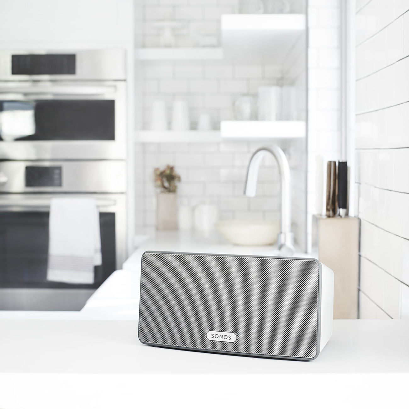 Ein weißer Sonos-Lautsprecher auf einer weißen Oberfläche in einer Küchenumgebung.