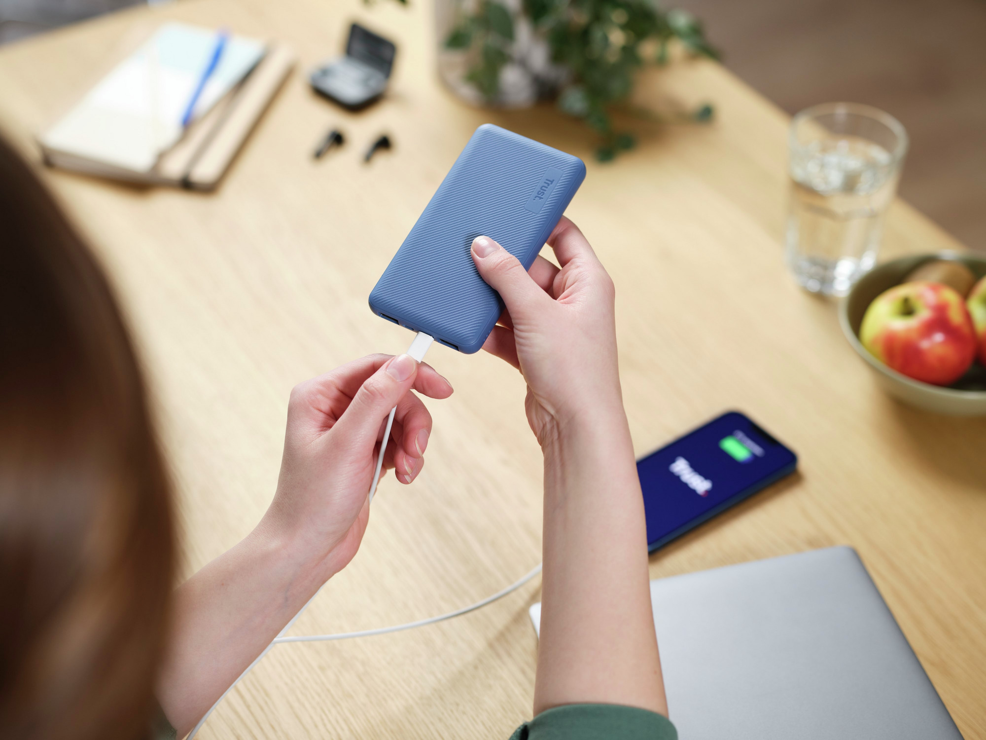 Frau lädt eine blaue Powerbank mit einem weißen Kabel auf einem Holztisch auf.