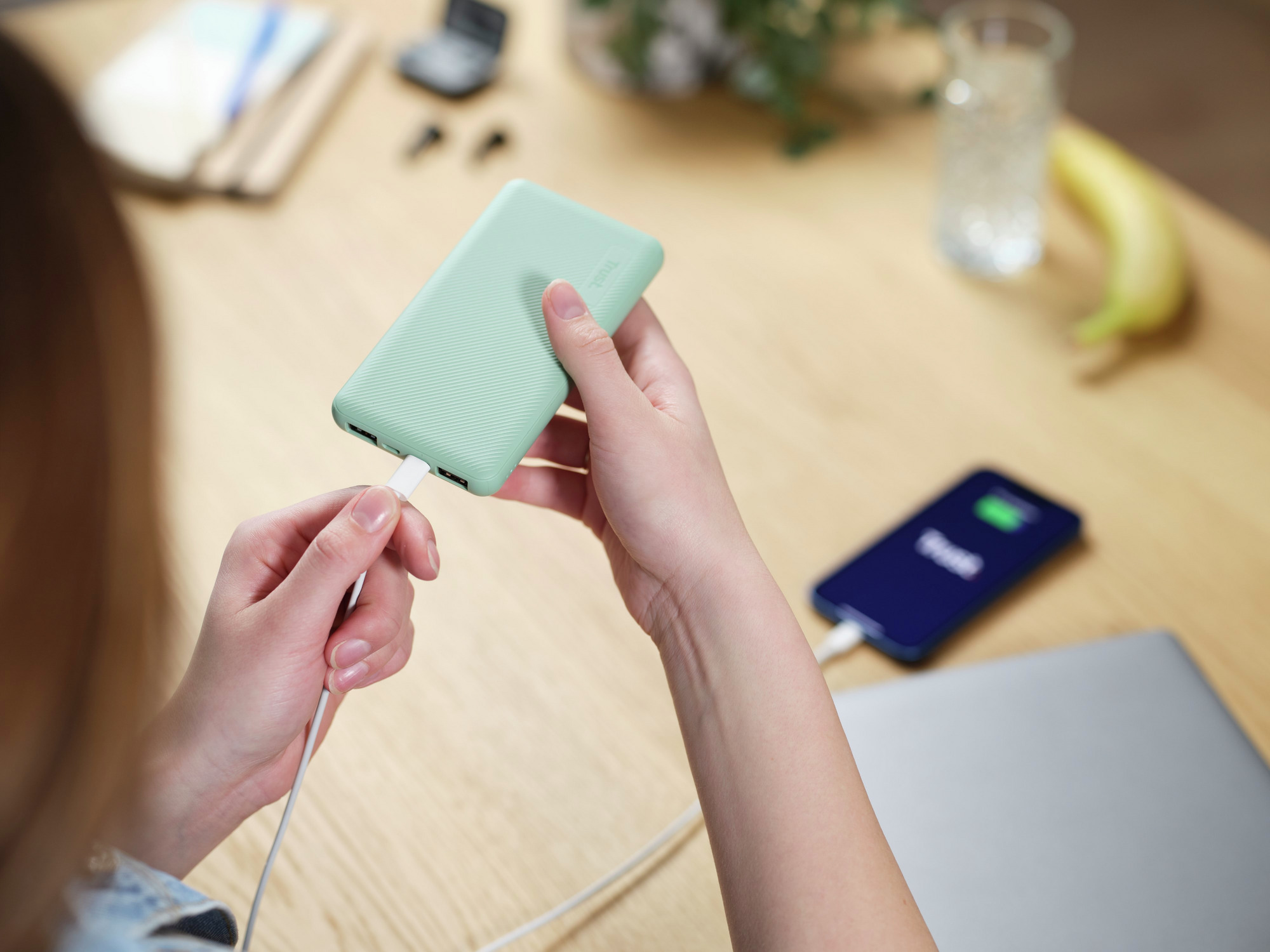 Een persoon die een witte kabel in een mintgroene powerbank steekt. Een telefoon is ook aangesloten.