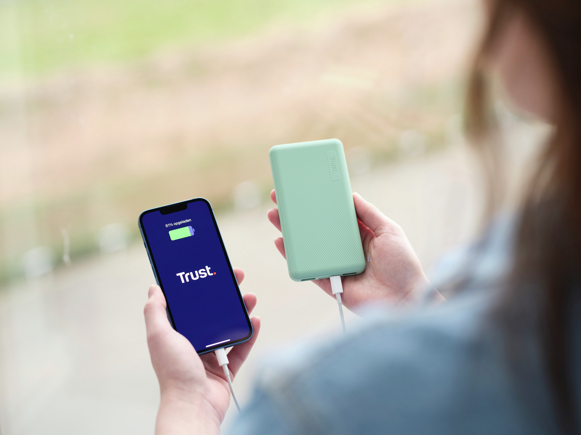 Een persoon die een telefoon en een powerbank vasthoudt en de telefoon oplaadt.