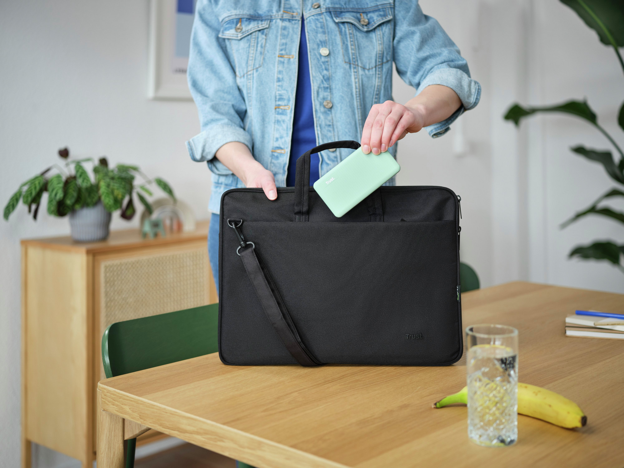 Persoon die een mintgroene telefoon in een zwarte laptoptas stopt.