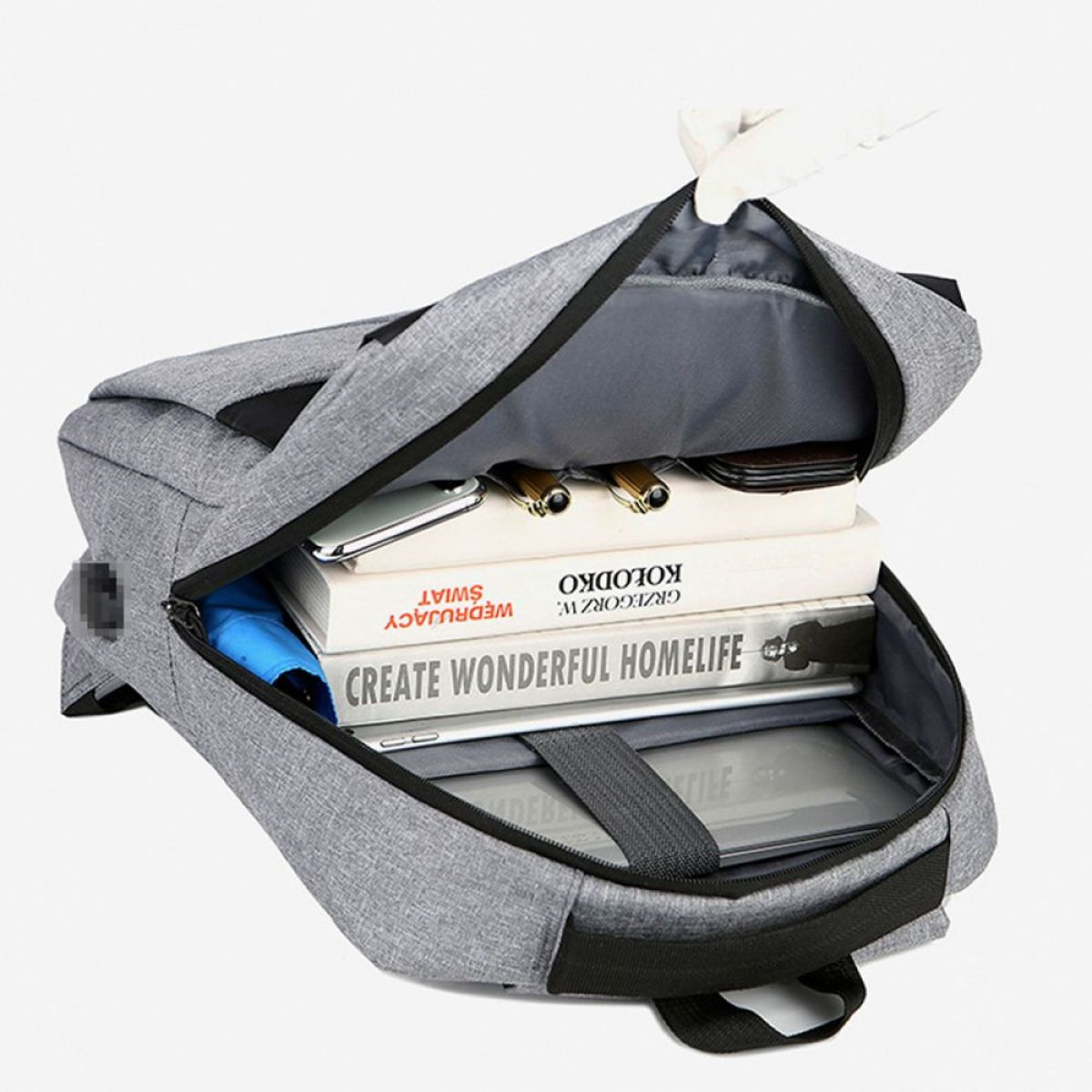 Grauer Rucksack mit Büchern, Tablet und anderen Gegenständen innen.