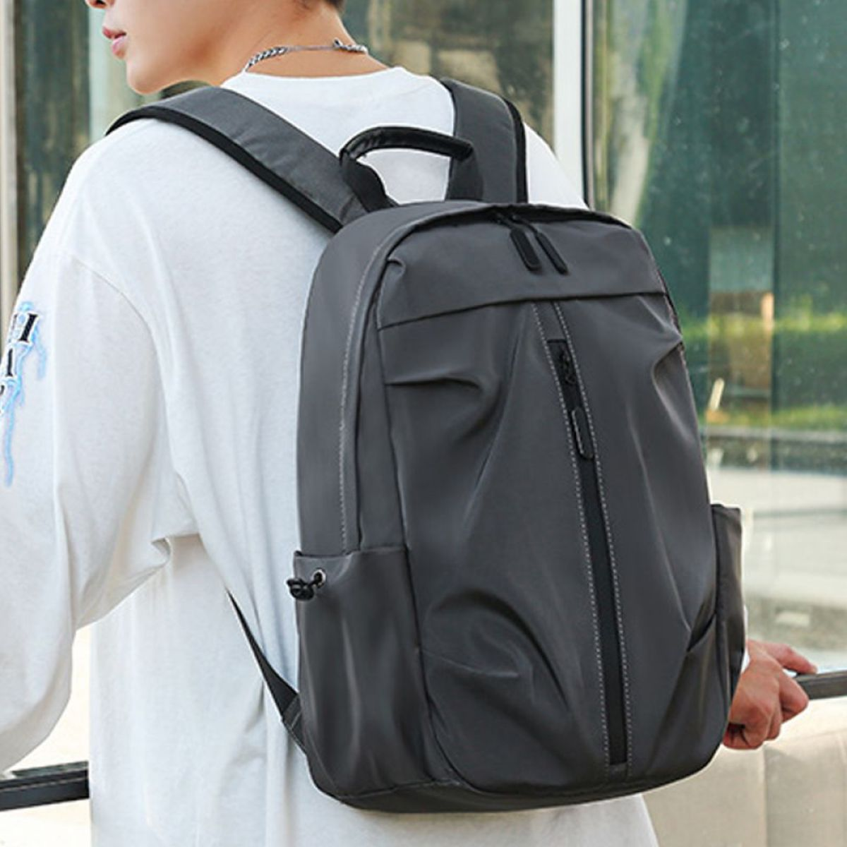 Person trägt weißes T-Shirt, hält grauen Rucksack mit Seitentaschen.