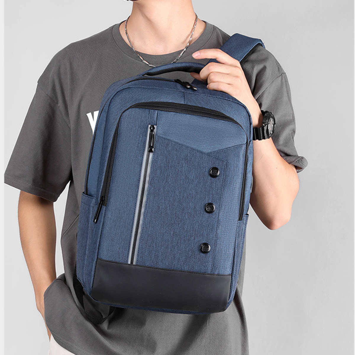 Ein Mann trägt einen blauen Rucksack mit blauem Hemd. Der Rucksack hat schwarze und silberne Details, vor grauem Hintergrund.