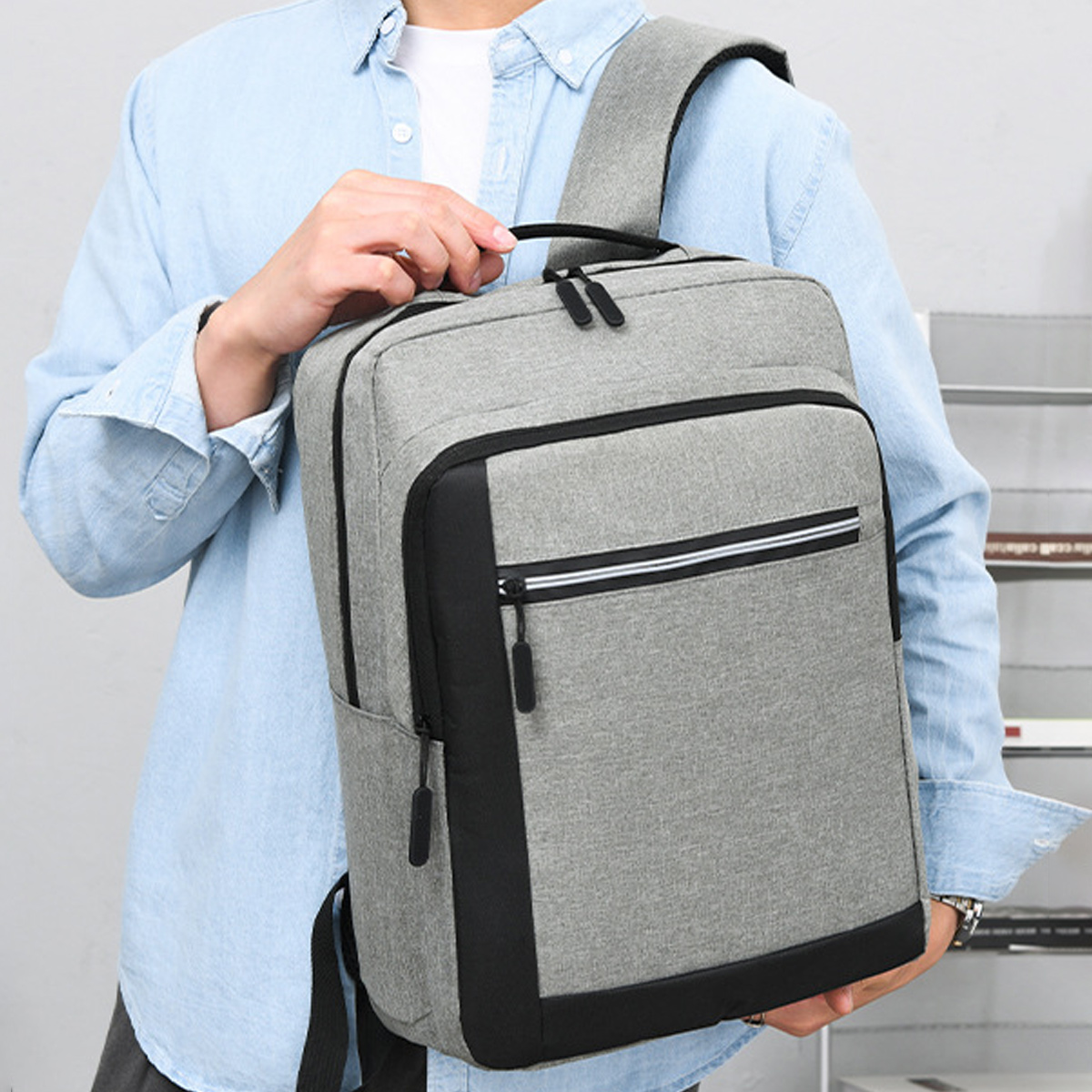Mann, der einen grauen Rucksack mit schwarzen Akzenten hält, hellblaues Hemd.