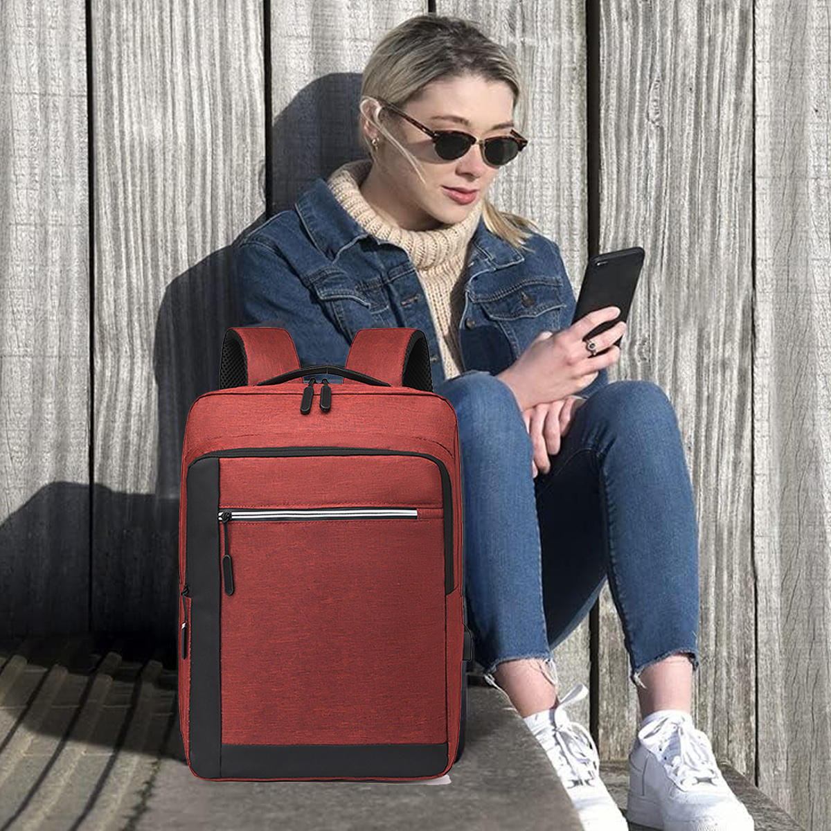 Eine Frau in Sonnenbrille und Jeansjacke sitzt mit rotem Rucksack. Holz Hintergrund.