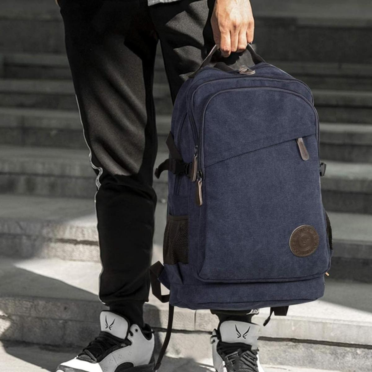 Person hält einen marineblauen Rucksack. Sie trägt schwarze Hosen und Turnschuhe auf einer Treppe.