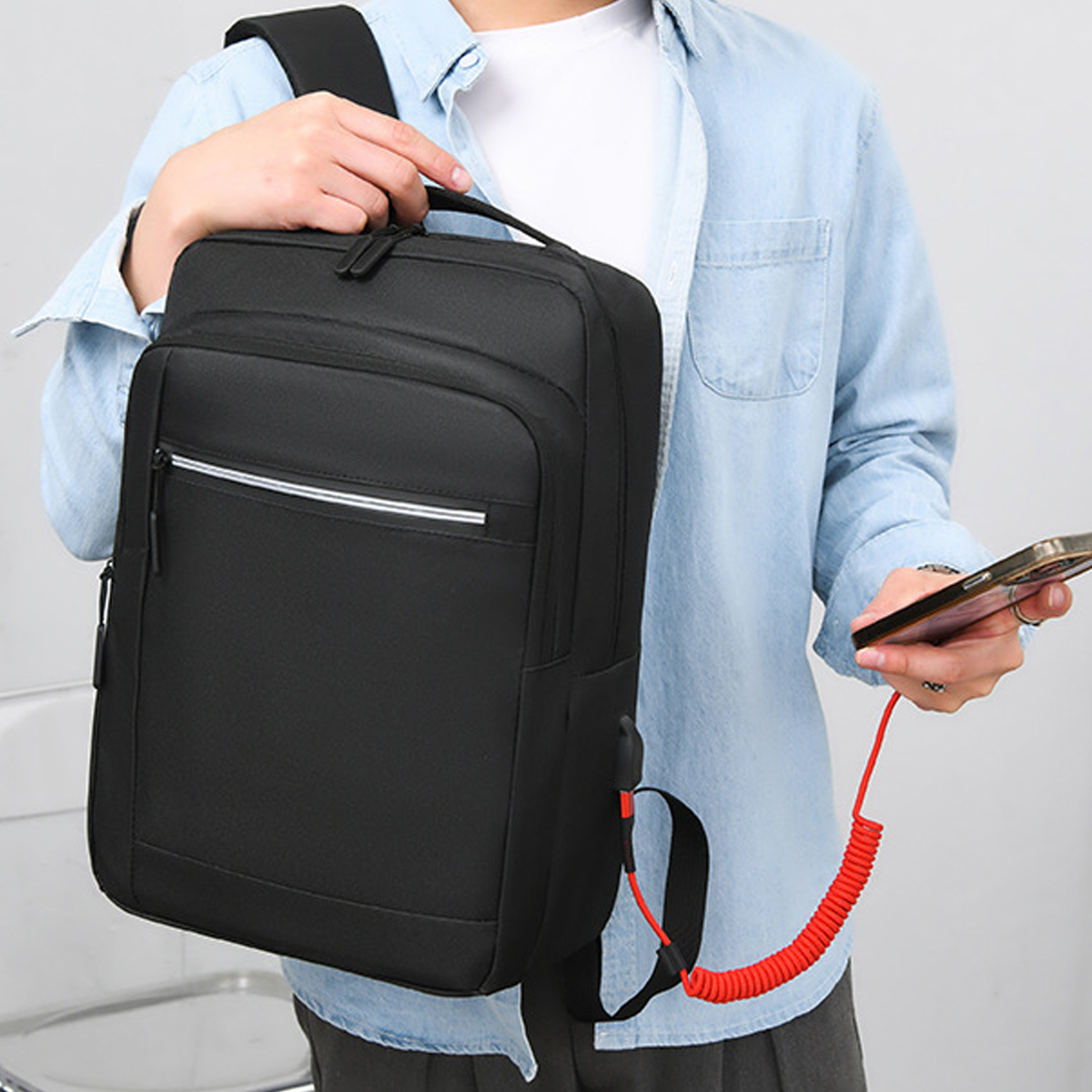 Person hält schwarzen Rucksack, Telefon mit rotem Ladekabel verbunden.