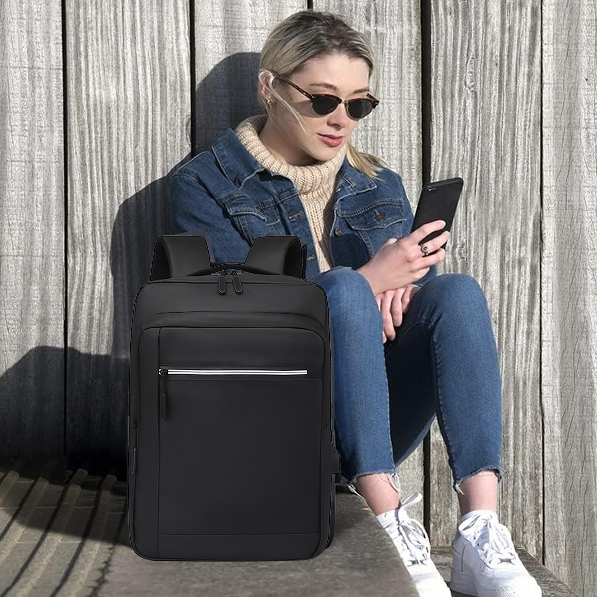 Eine Frau mit Sonnenbrille und Rucksack sitzt an einer Holzwand und benutzt ein Telefon.