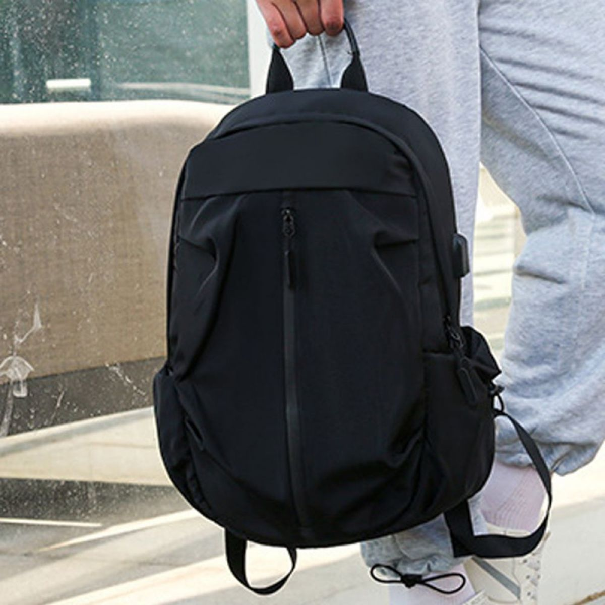 Schwarzer Rucksack, Mann hält den Griff vor einem Fenster.