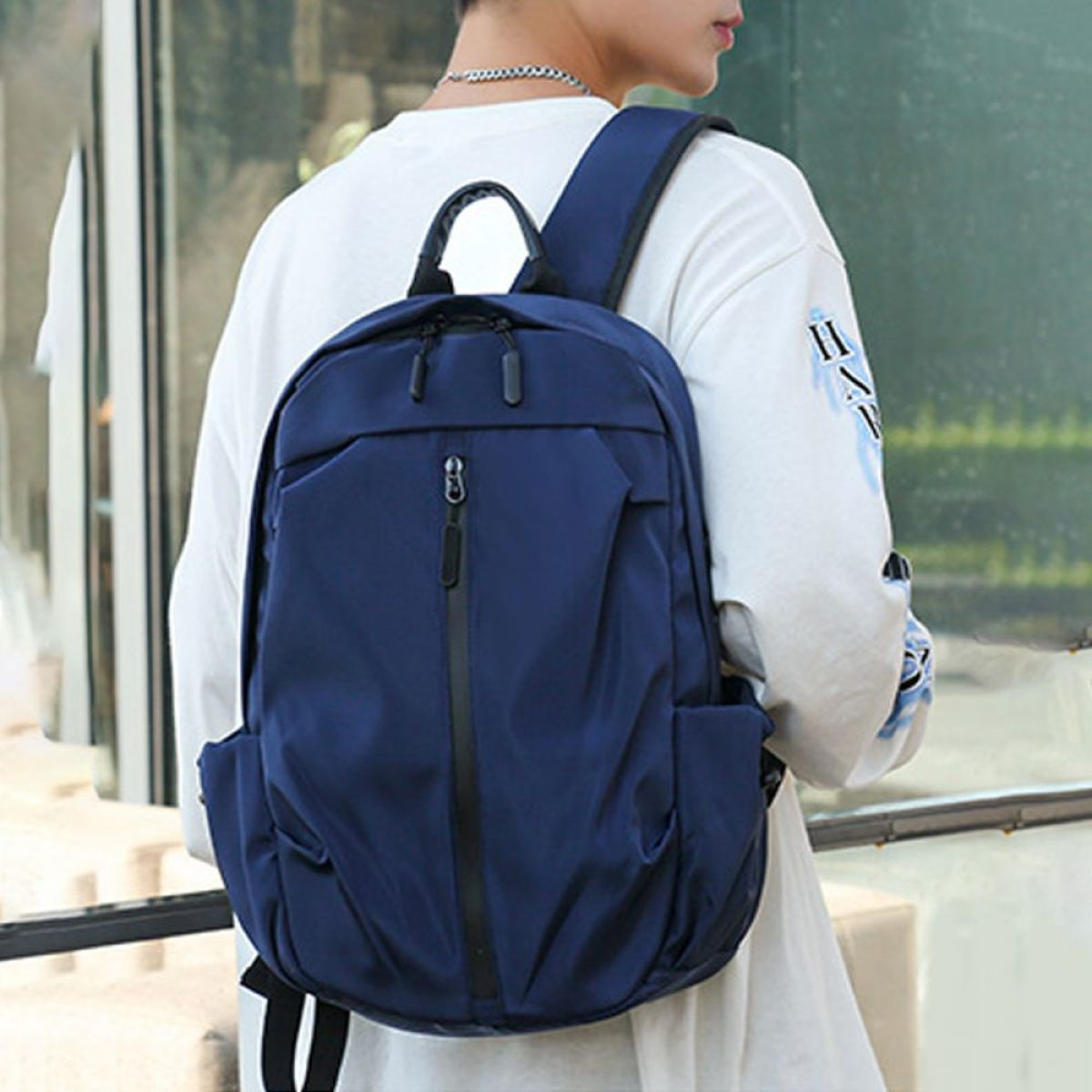 Ein Mann in weißem Hemd mit marineblauem Rucksack, von hinten gesehen. Der Rucksack hat Taschen.