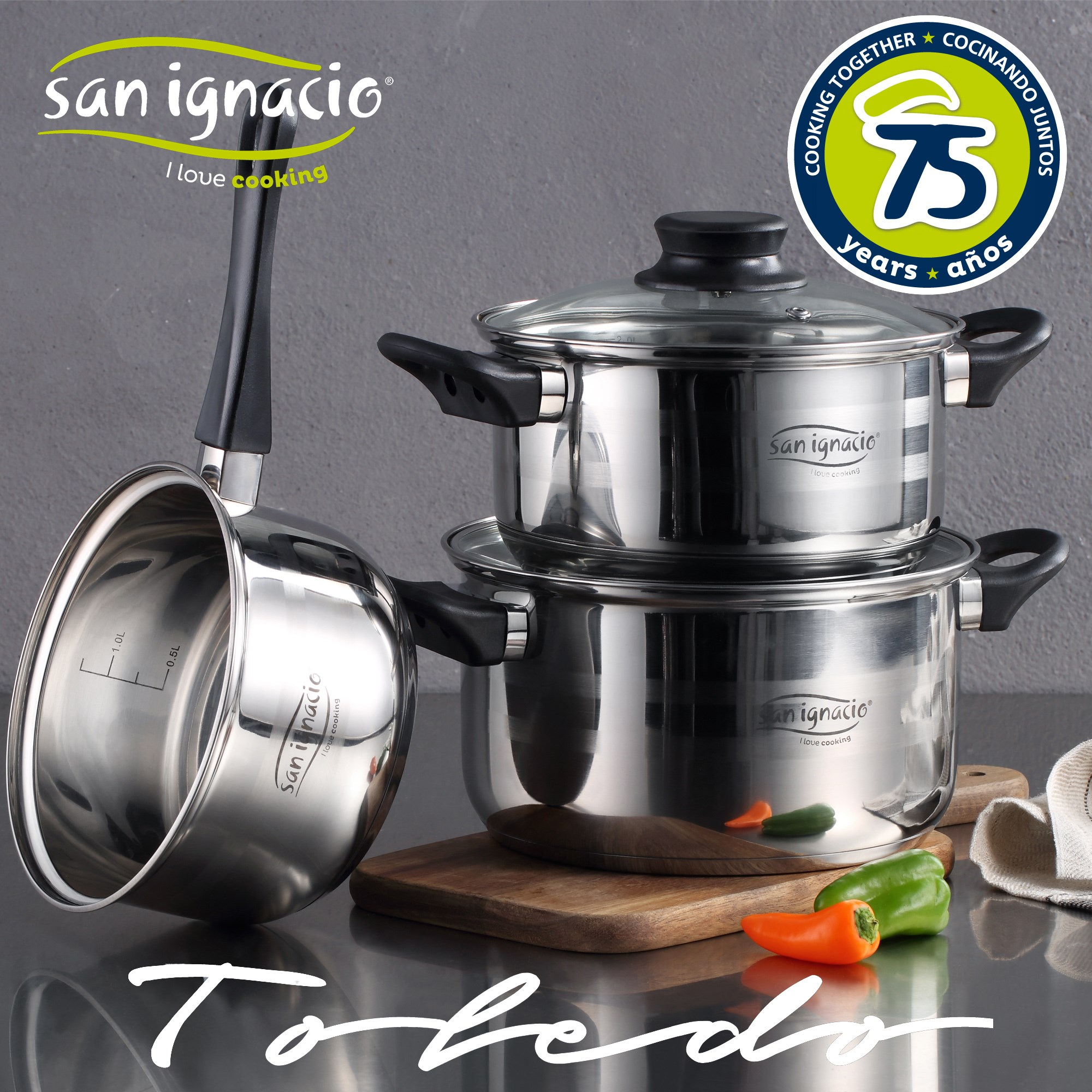 Juego de utensilios de cocina de acero inoxidable, incluye ollas y un cucharón. Sobre una mesa, con pimientos y una tabla de madera.