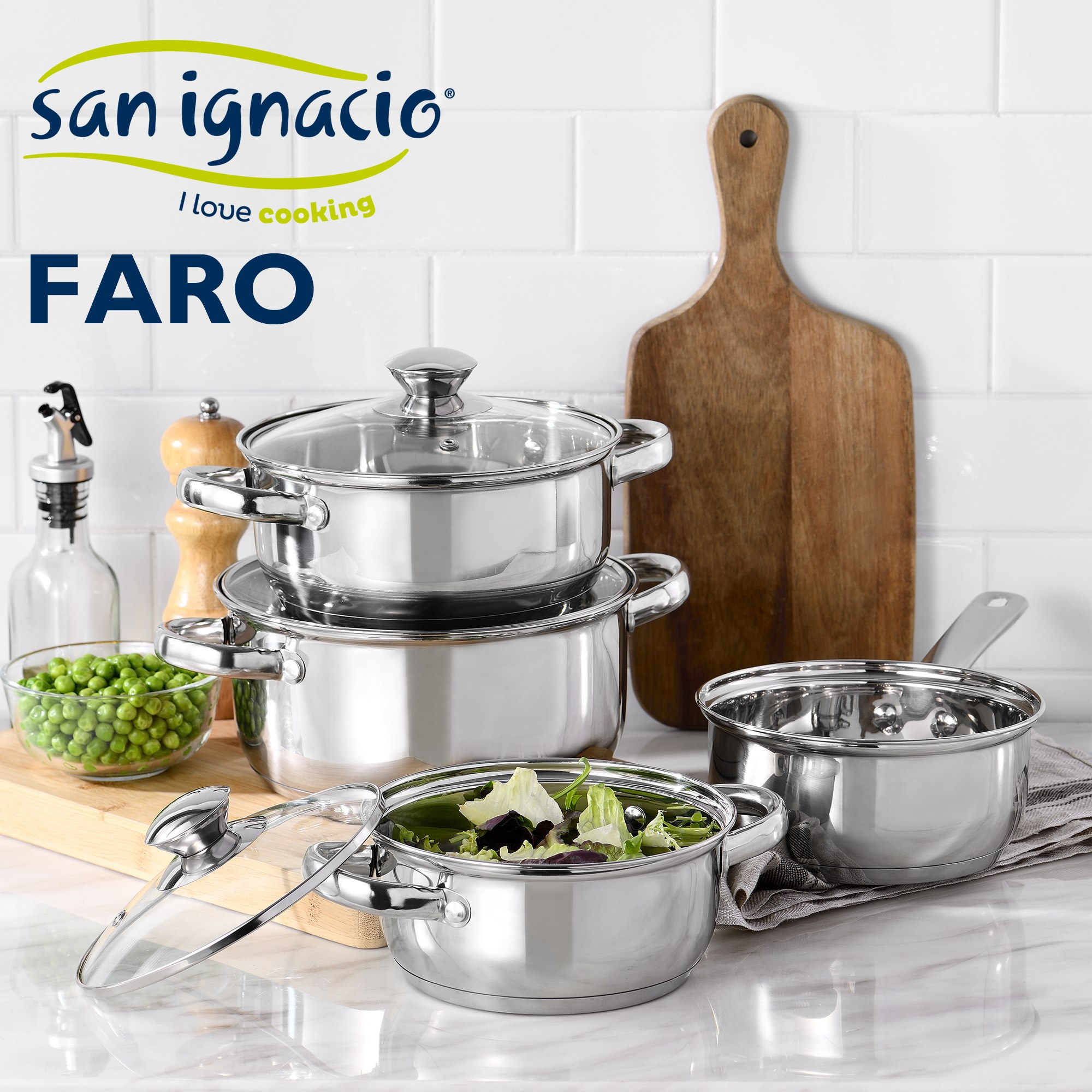 Ollas de acero inoxidable sobre superficie de mármol. Tabla de cortar e ingredientes a la izq.