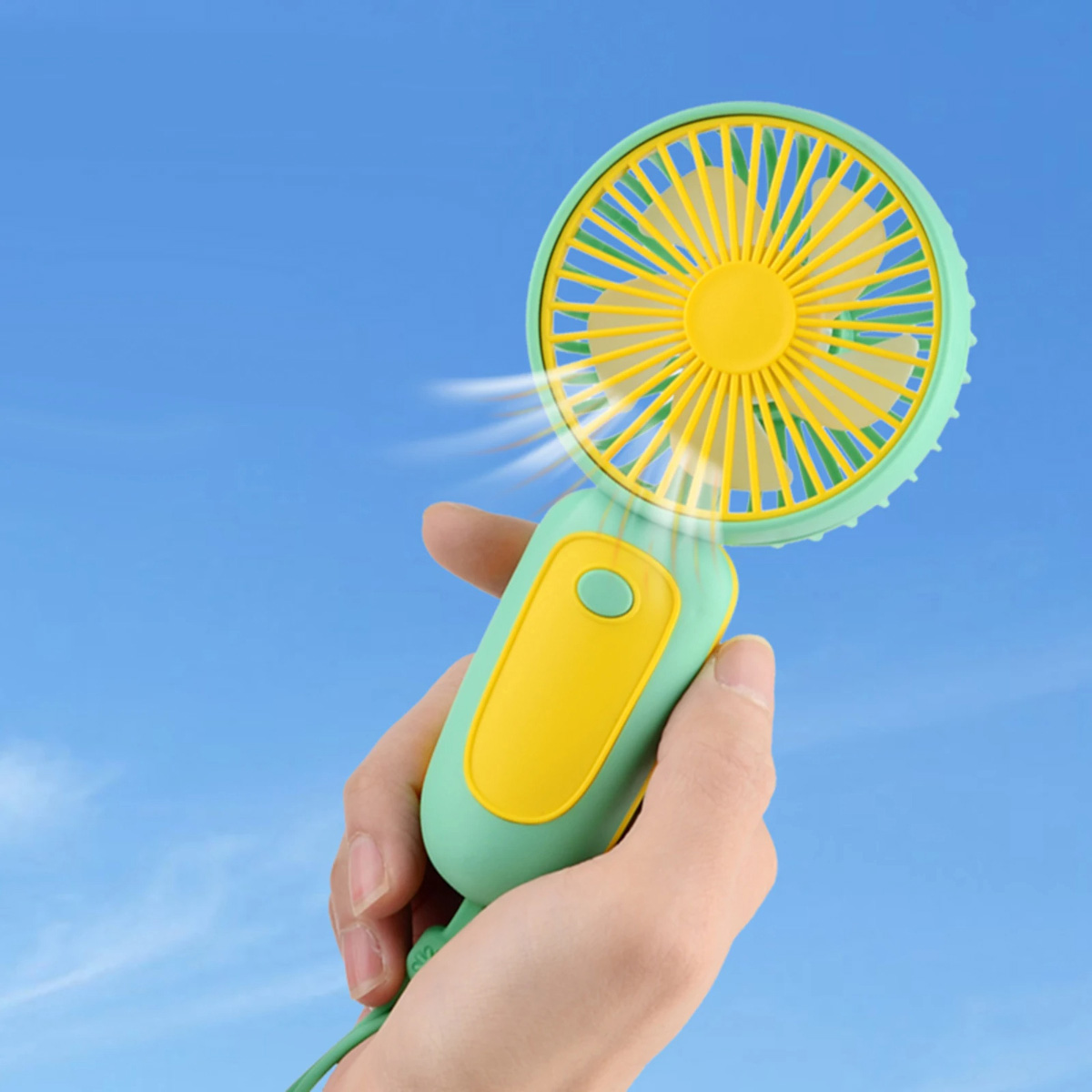Ventilador de mano con colores verde y amarillo. Fondo de cielo azul.