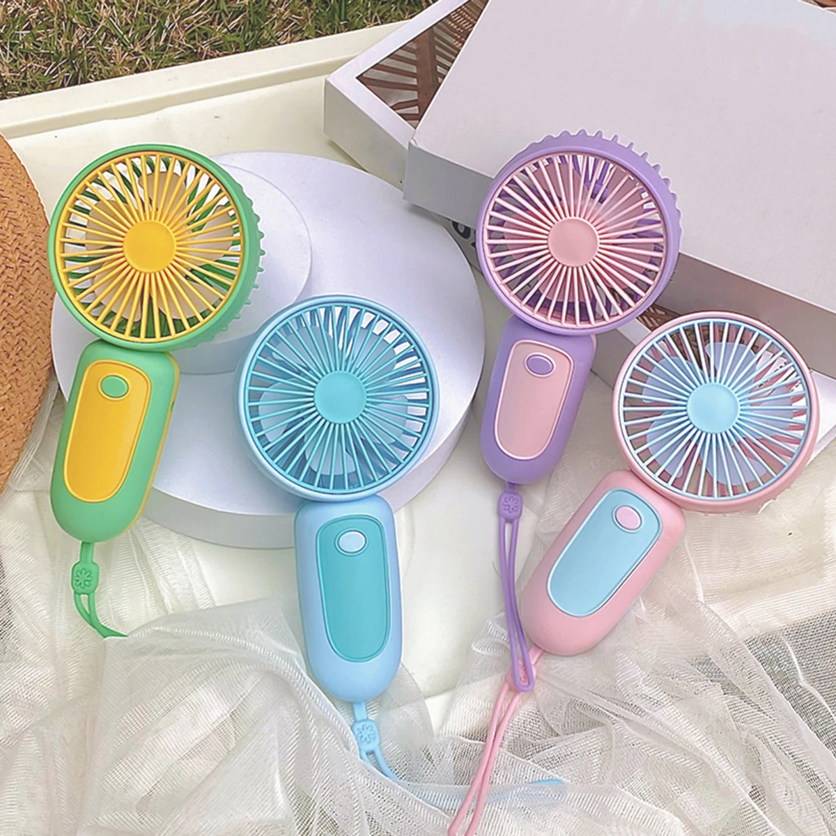 Seis mini ventiladores de mano coloridos, sobre una superficie blanca con vegetación.