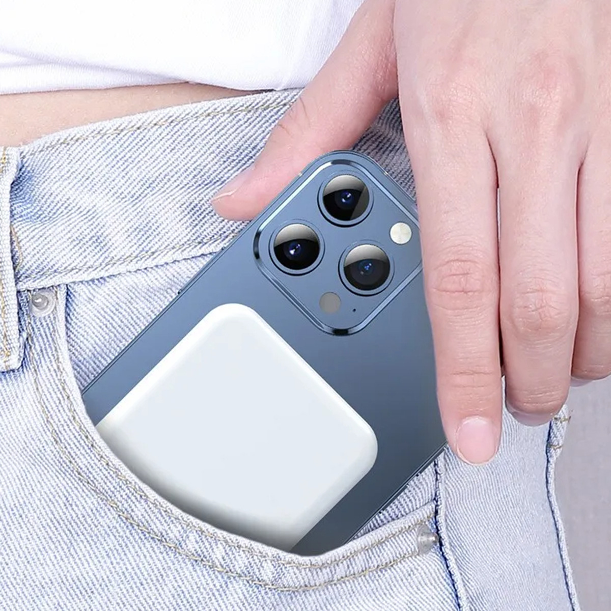Una mano sostiene un teléfono en un bolsillo de jean con una almohadilla de carga blanca adjunta al teléfono.