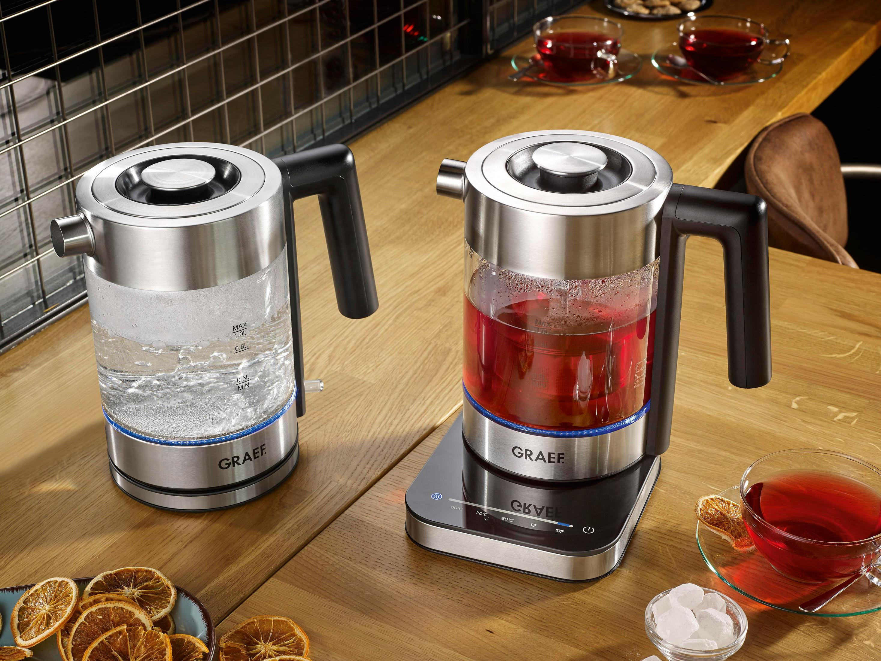 Dwa czajniki ze stali nierdzewnej z czarnymi uchwytami. Jeden czajnik ma wodę, drugi czerwoną herbatę.