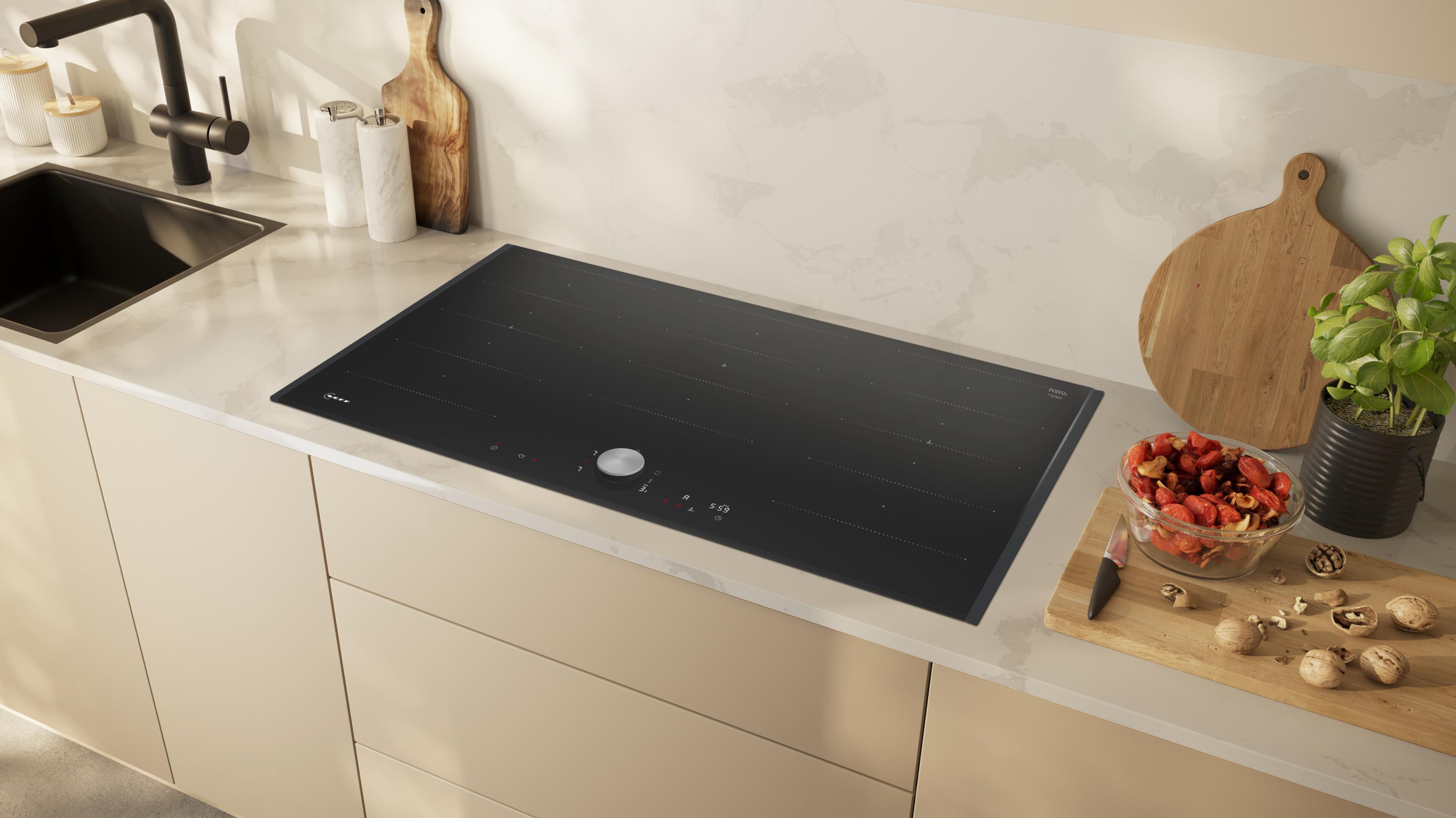 Czarna płyta indukcyjna na blacie z deską do krojenia, składnikami i przyborami kuchennymi.