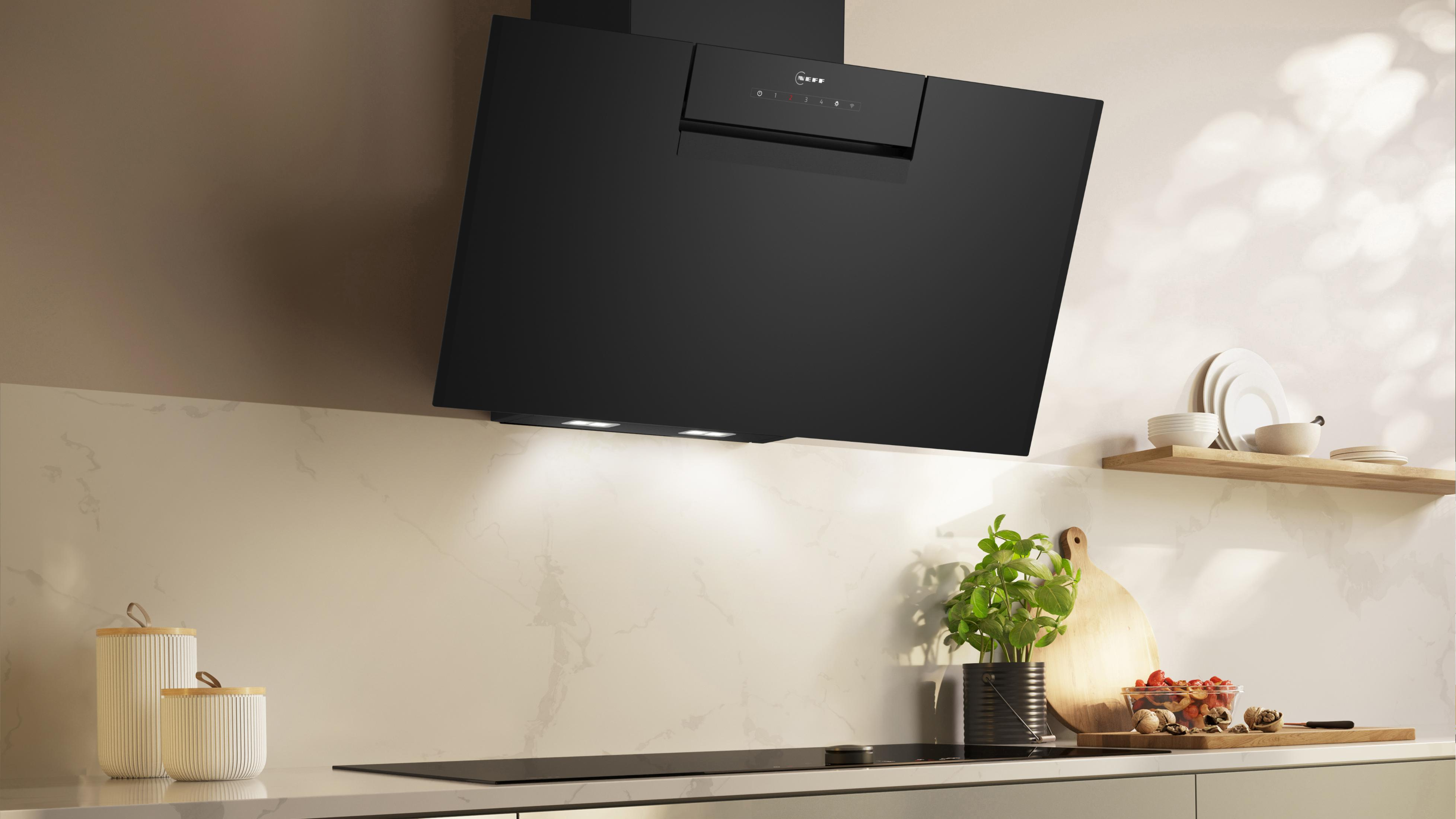 Cappa da cucina nera con piano di lavoro bianco, piano cottura nero e mensola in legno con oggetti.