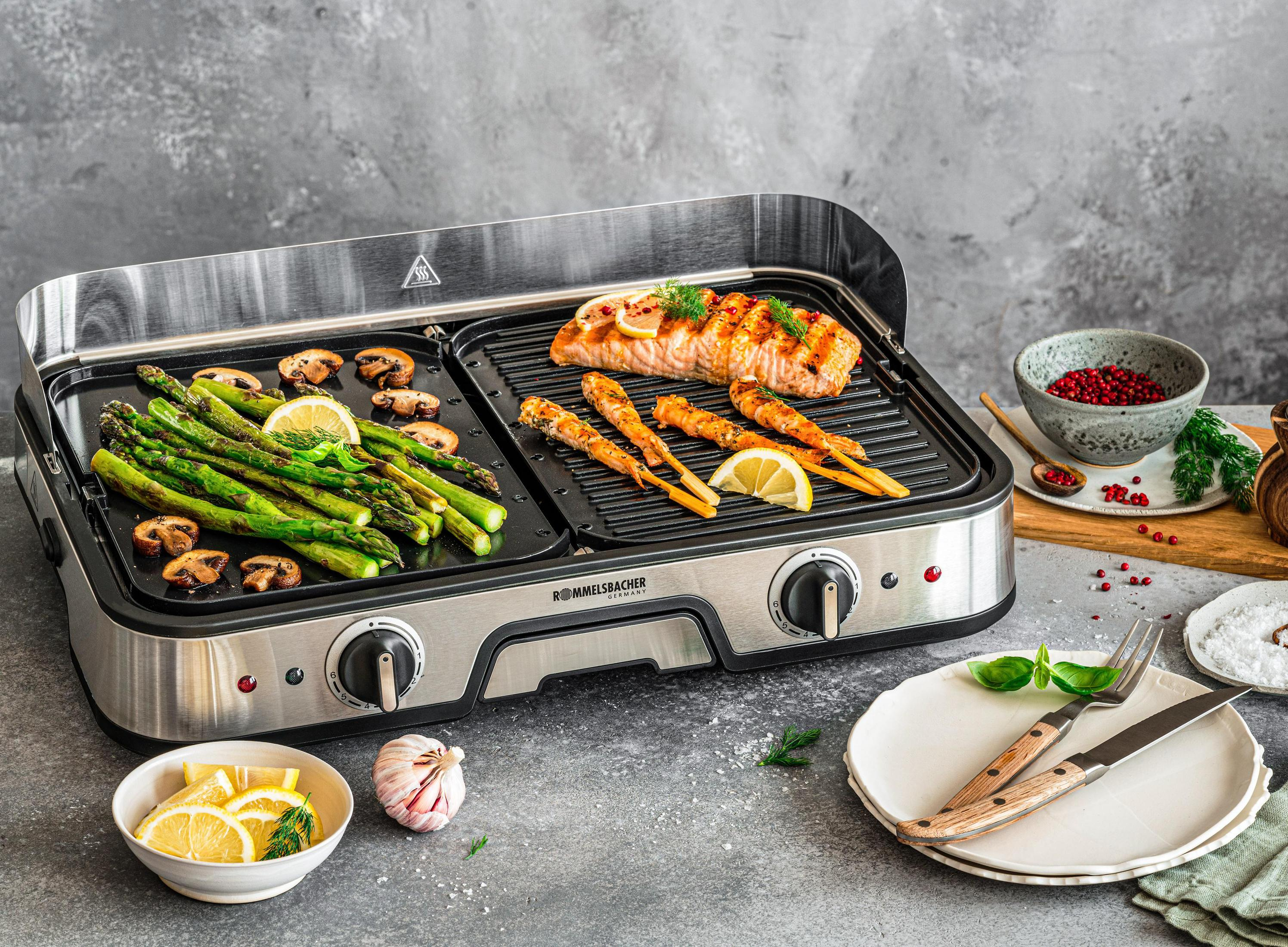 Grill with food, including salmon, asparagus, and shrimp. Plates with lemons and seasonings.