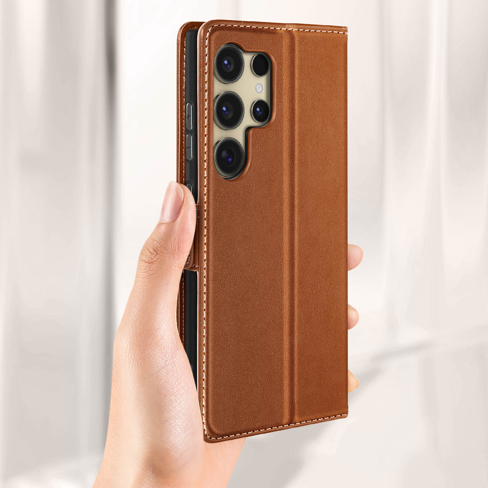 Mano che tiene custodia in pelle marrone con telefono dentro. Cuciture bianche visibili.