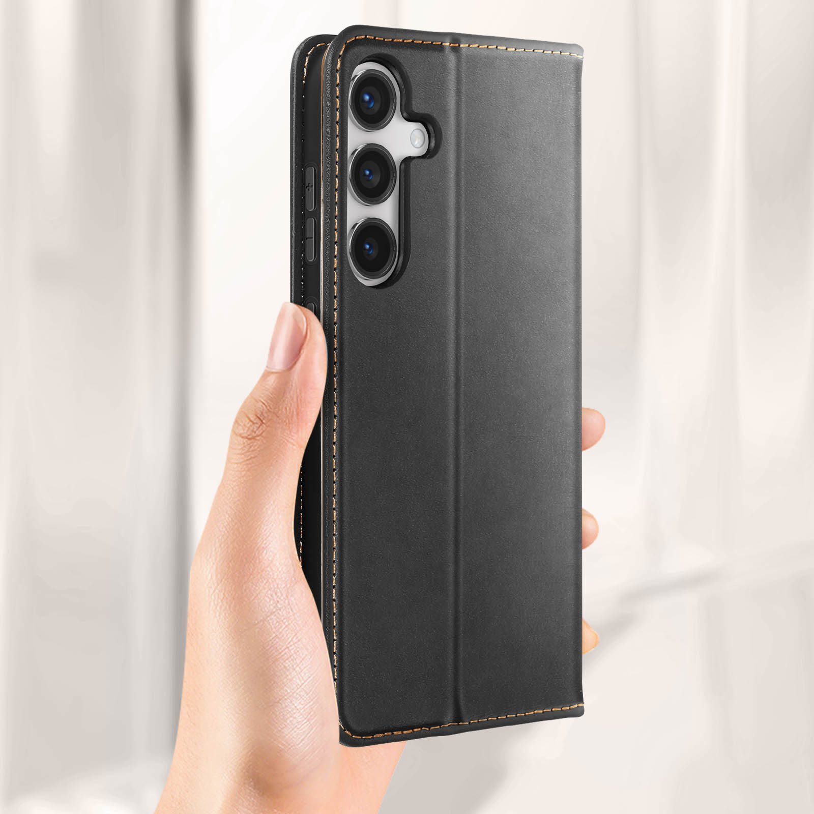 Una mano che tiene una custodia nera con un telefono. Cuciture dorate visibili.