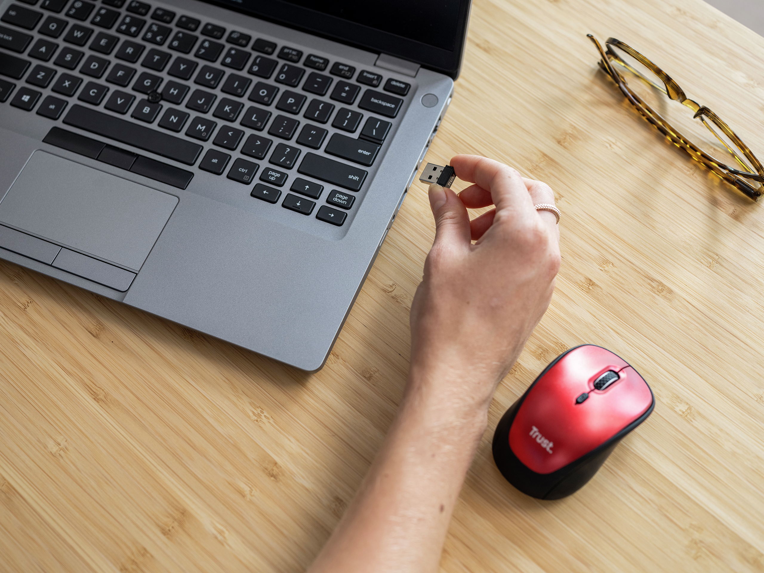 Ręka osoby wkładająca pendrive do laptopa. Czerwona mysz znajduje się po prawej stronie.