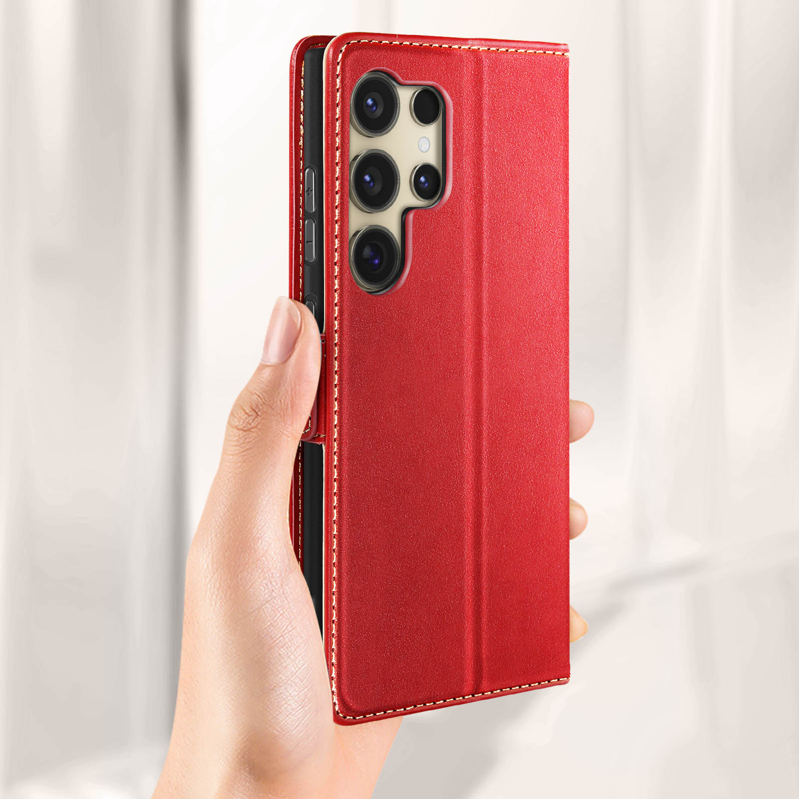 Eine Hand hält eine rote Handyhülle mit einem Telefon darin. Weiße Nähte auf der Hülle. Weißer Hintergrund.