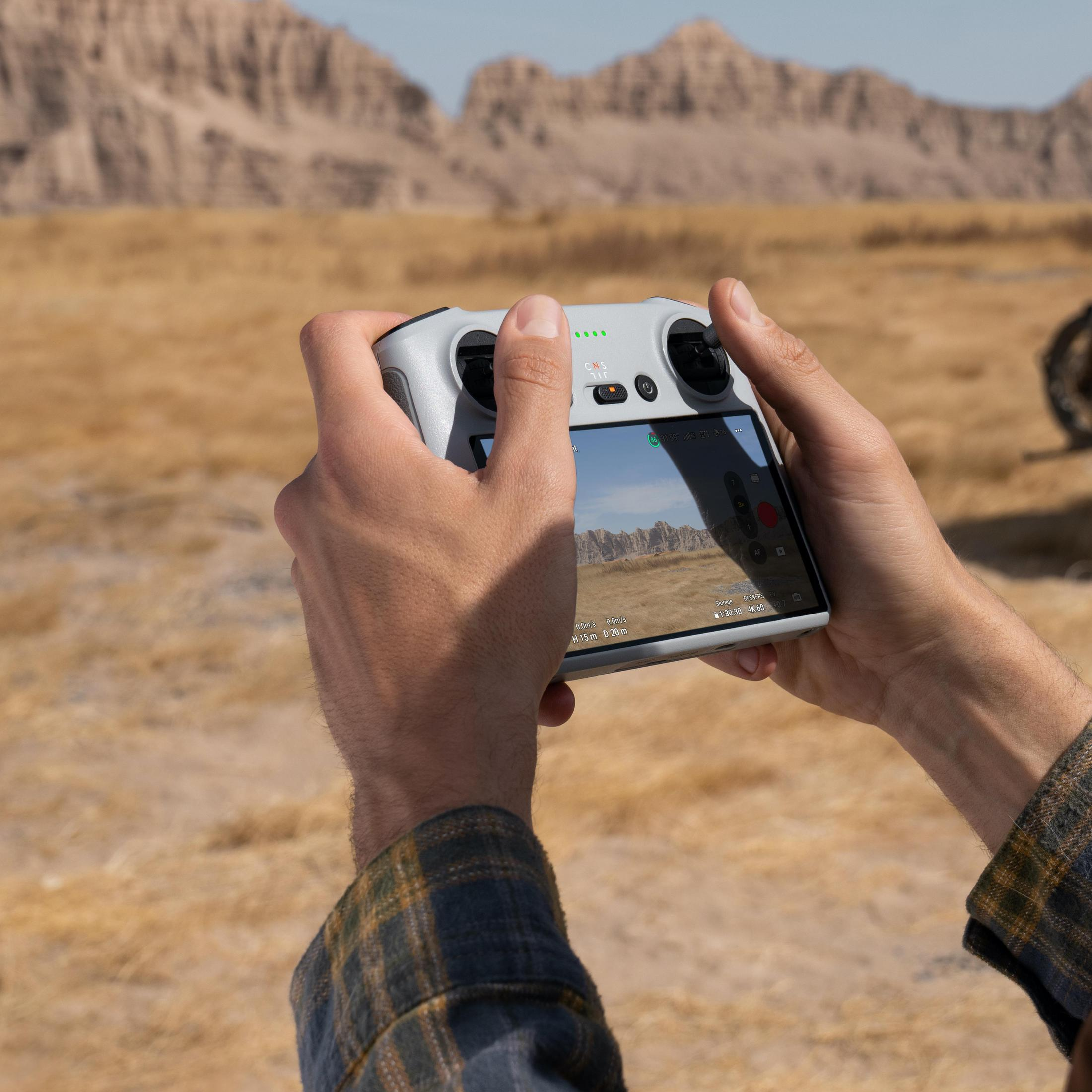 Eine Person hält eine Drohnensteuerung, Wüste im Hintergrund. Der Controller-Bildschirm ist sichtbar.
