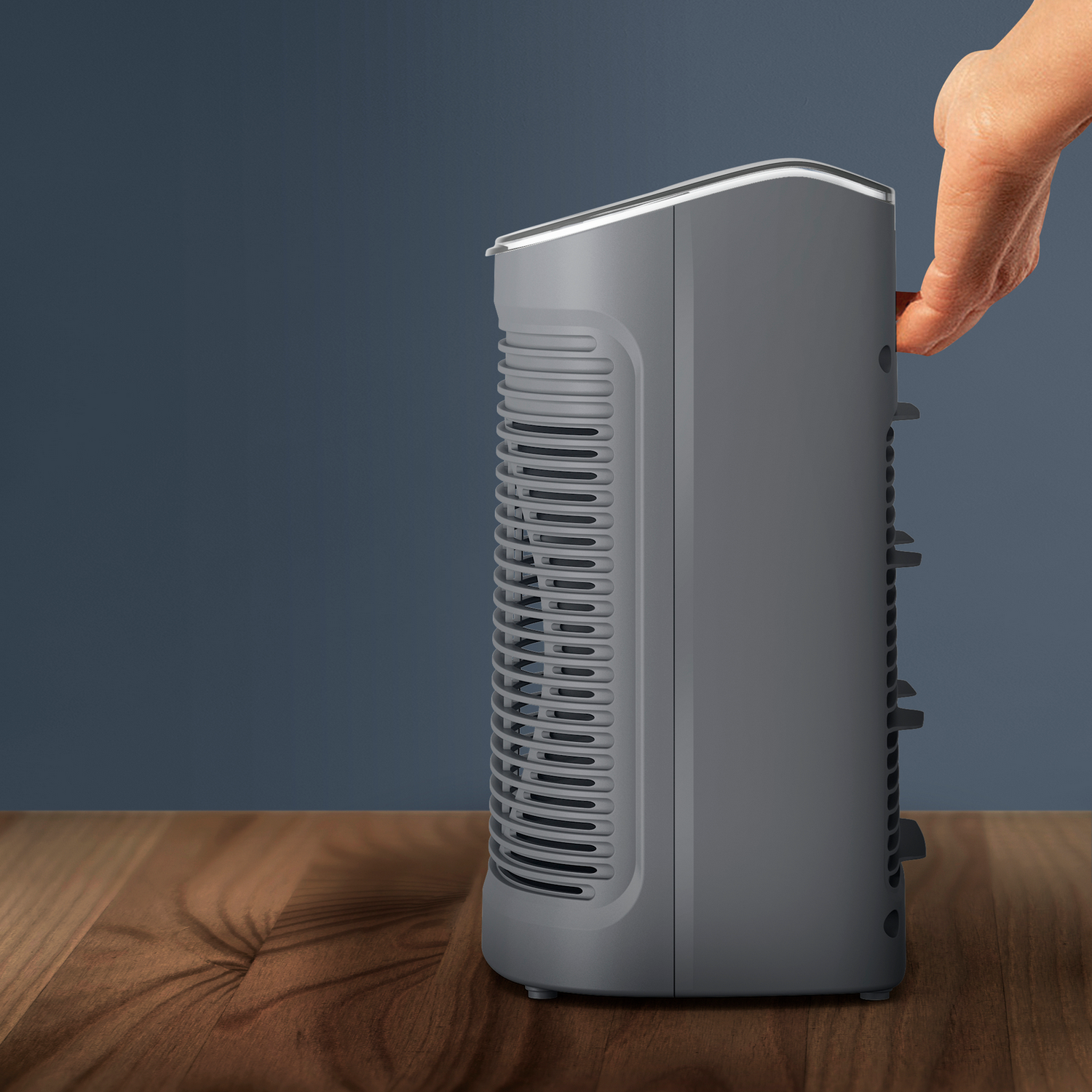 Szary oczyszczacz powietrza na drewnianej powierzchni. Dłoń sięga do boku urządzenia.