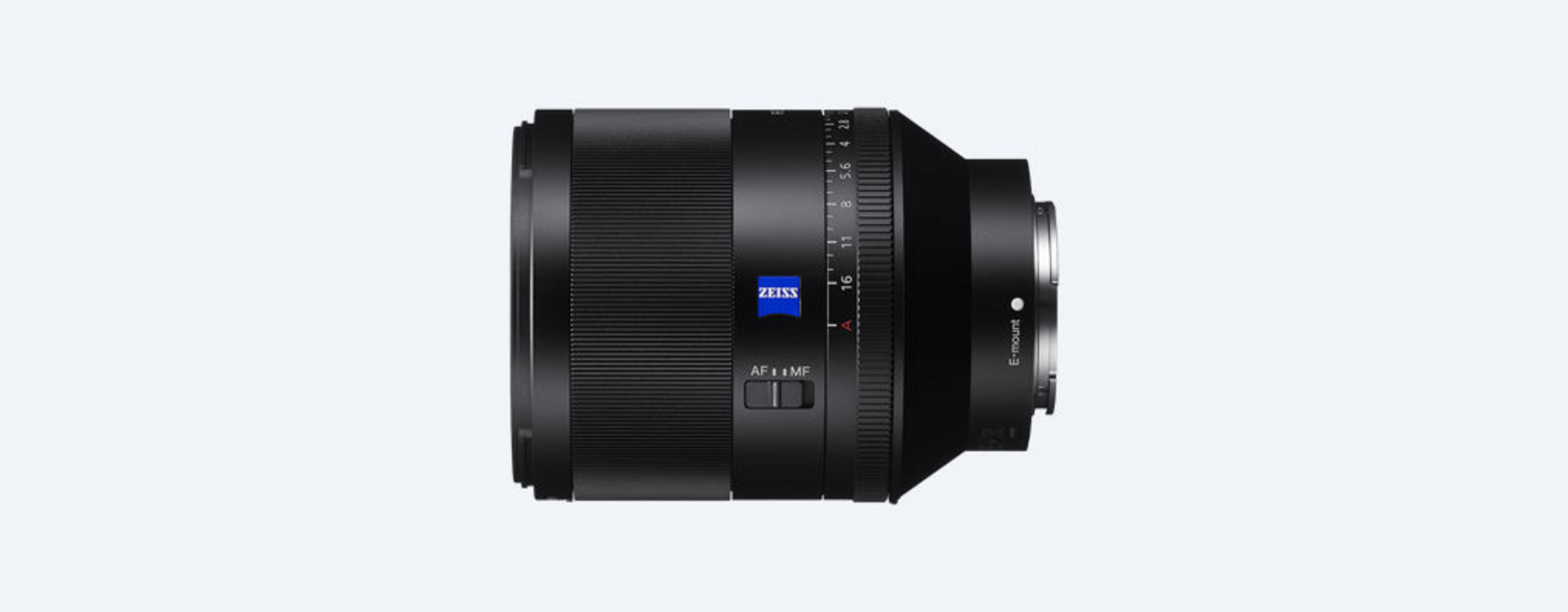 Lente de cámara Zeiss negro, vista lateral, con logo azul de Zeiss. Lente sobre fondo blanco.