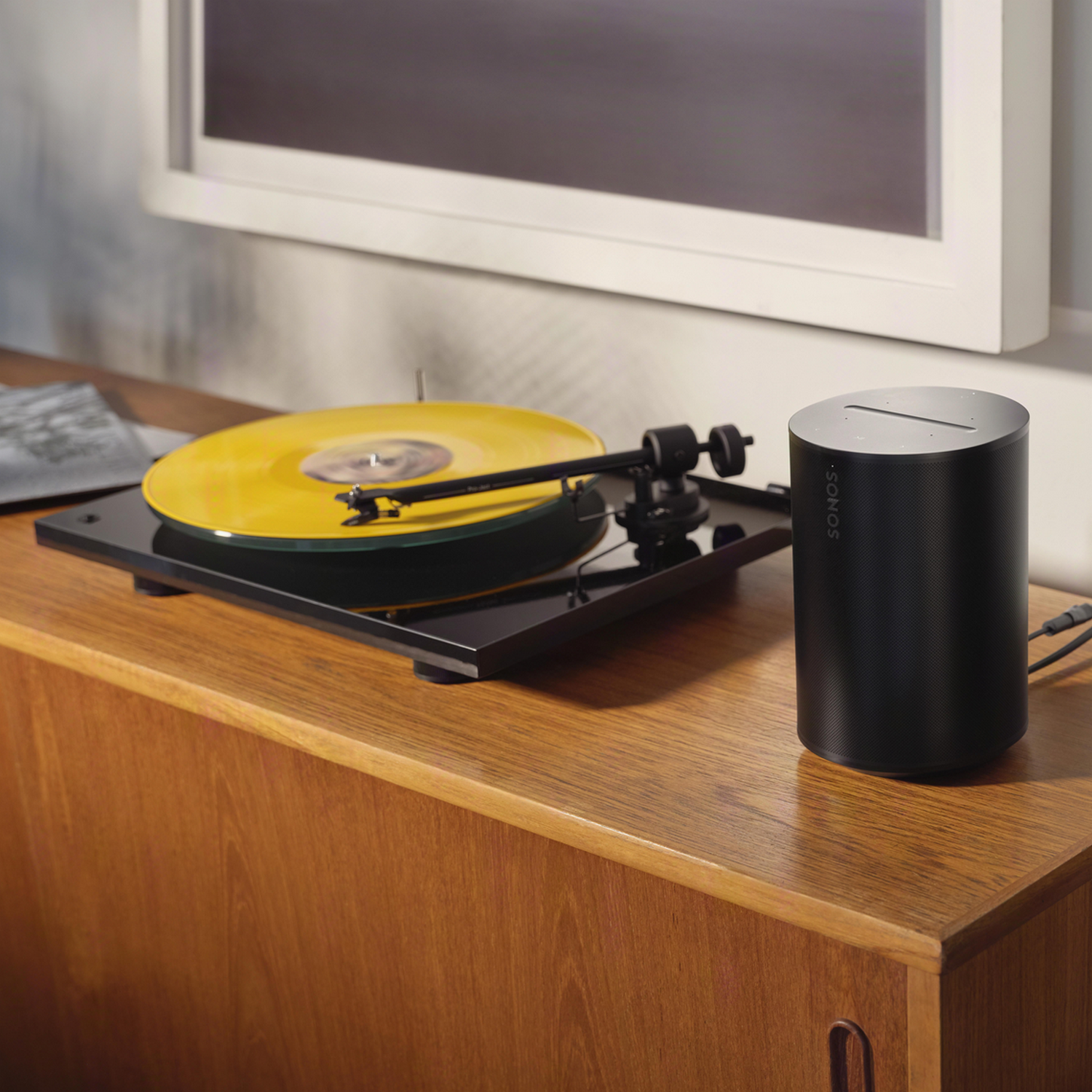 Gramofon z żółtą płytą i czarnym głośnikiem na drewnianej szafce.